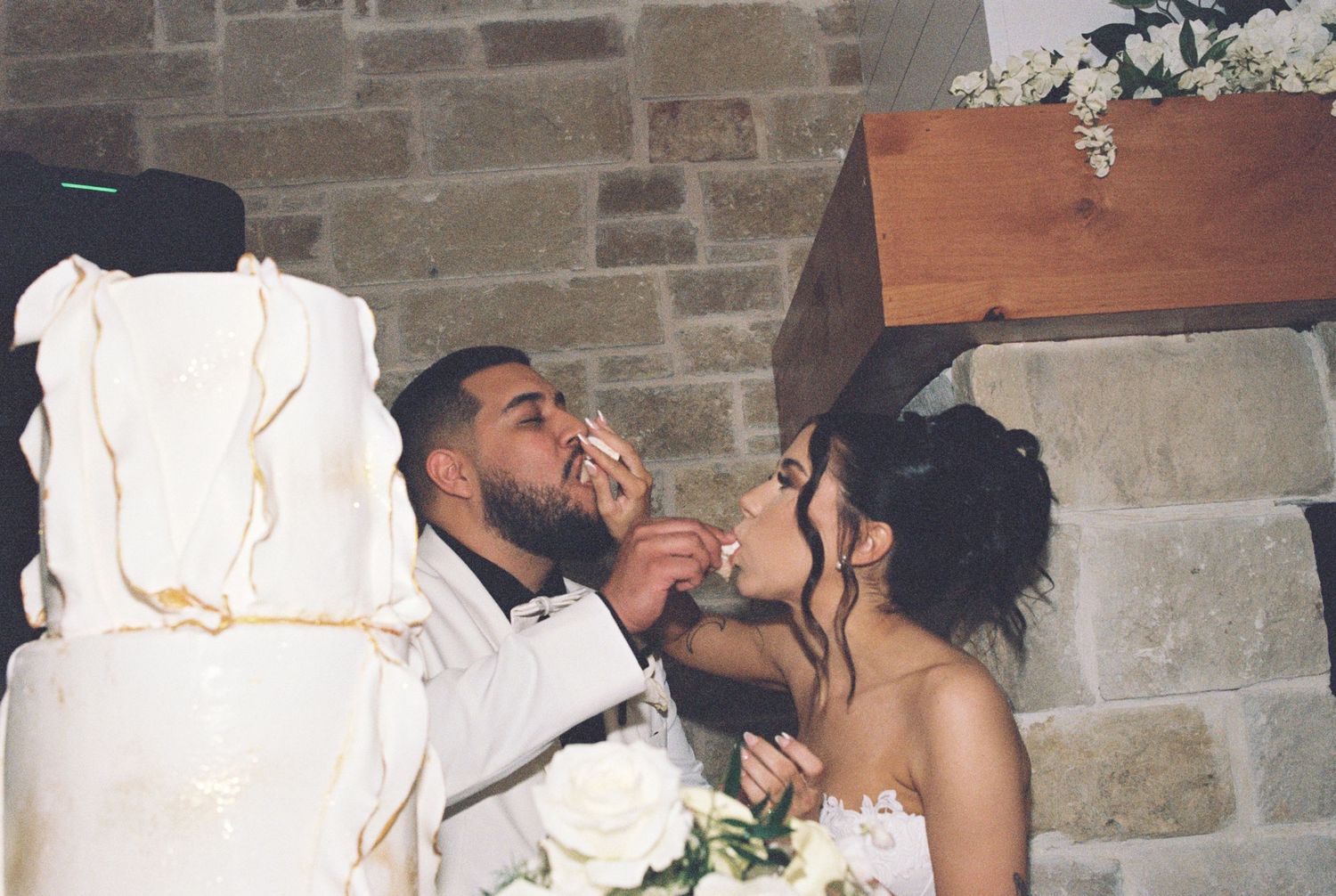 A joyful newlywed couple sharing a playful moment while cutting their elegant white wedding cake.