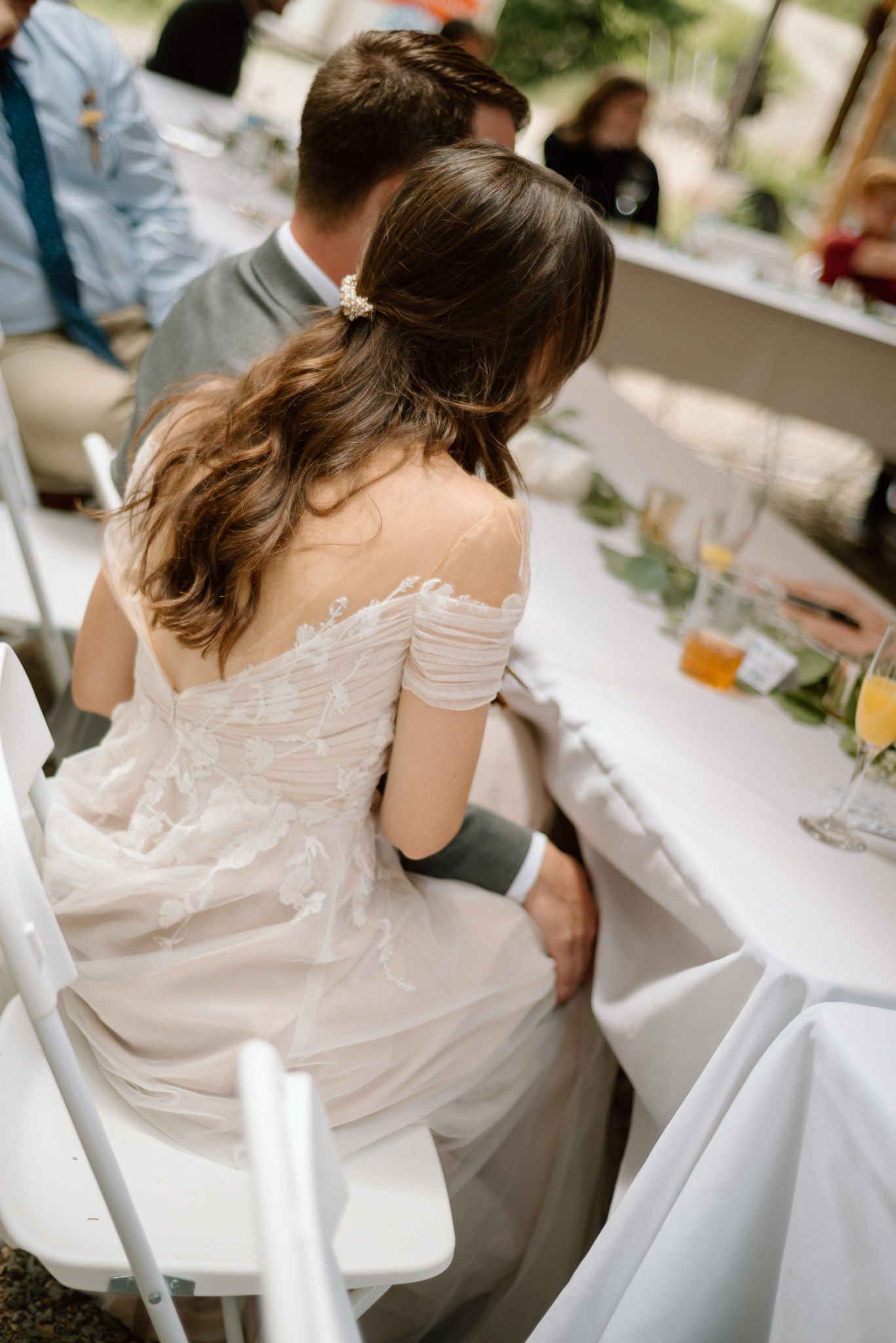 A bride in an off-shoulder wedding dress sits at a reception table.