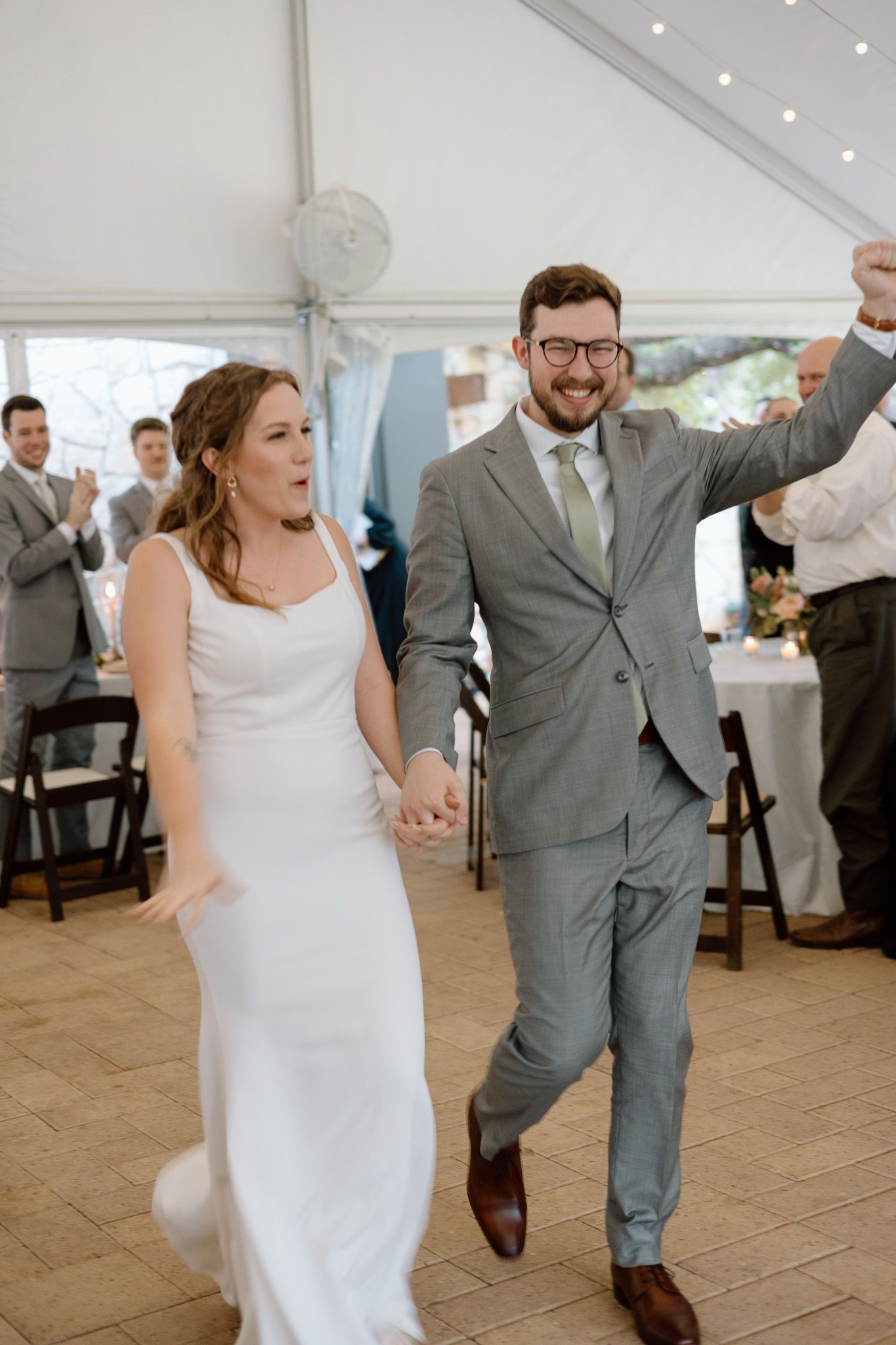 Newlyweds dancing and celebrating in a tent reception venue with wooden floors.