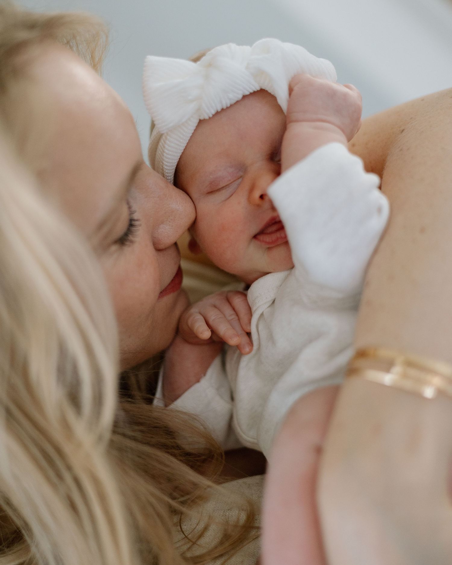 Tender moment between mother and sleeping newborn in white clothing.