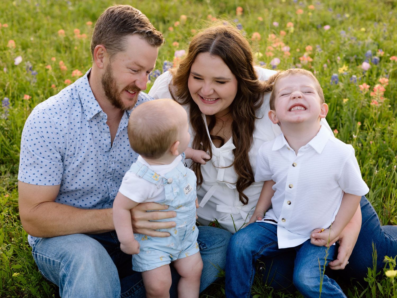 A cheerful family sits together in a wildflower meadow on a sunny day sharing joyful laughter.