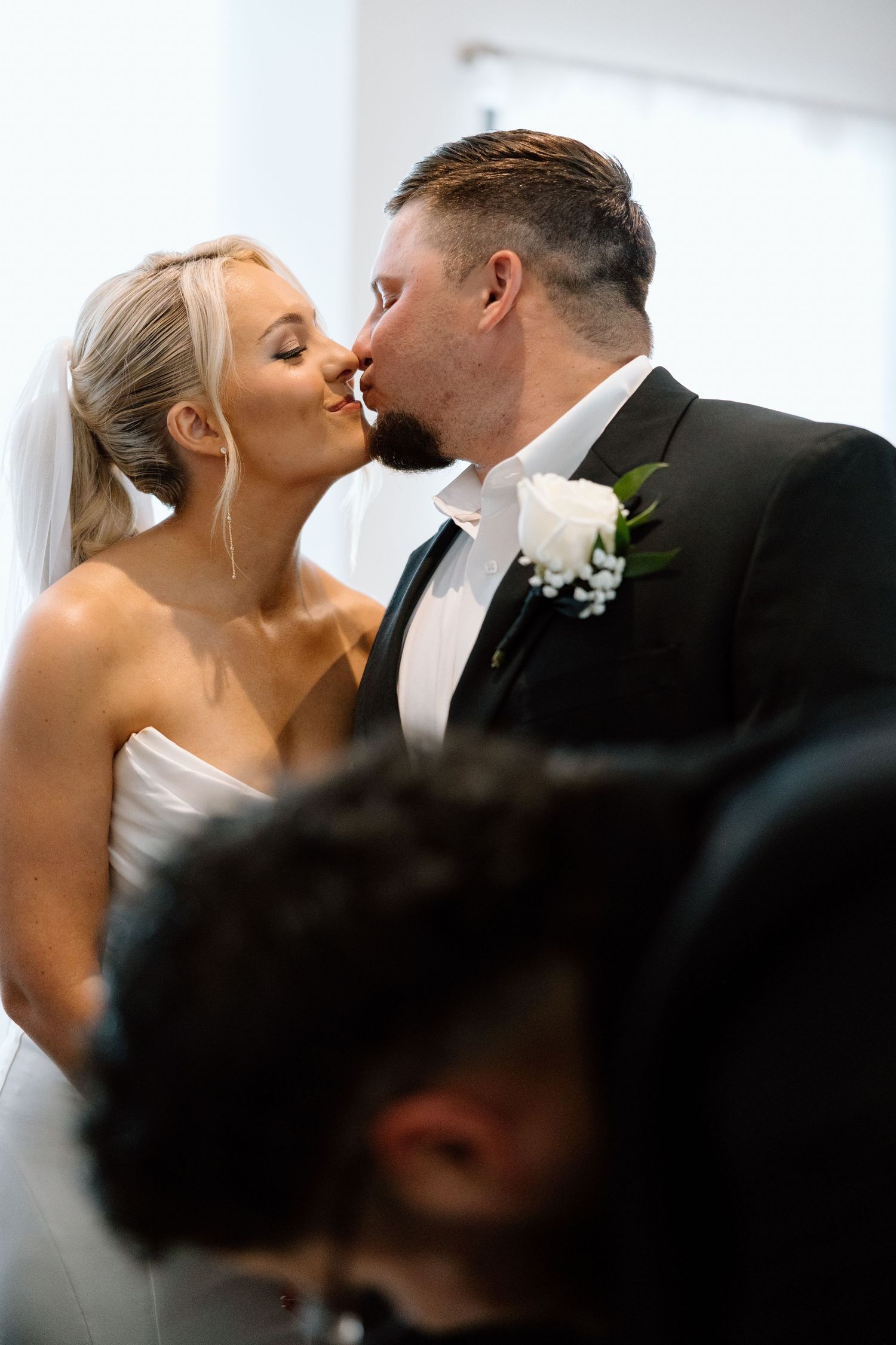 Bride and groom share first kiss as newlyweds during wedding ceremony before seated guests.