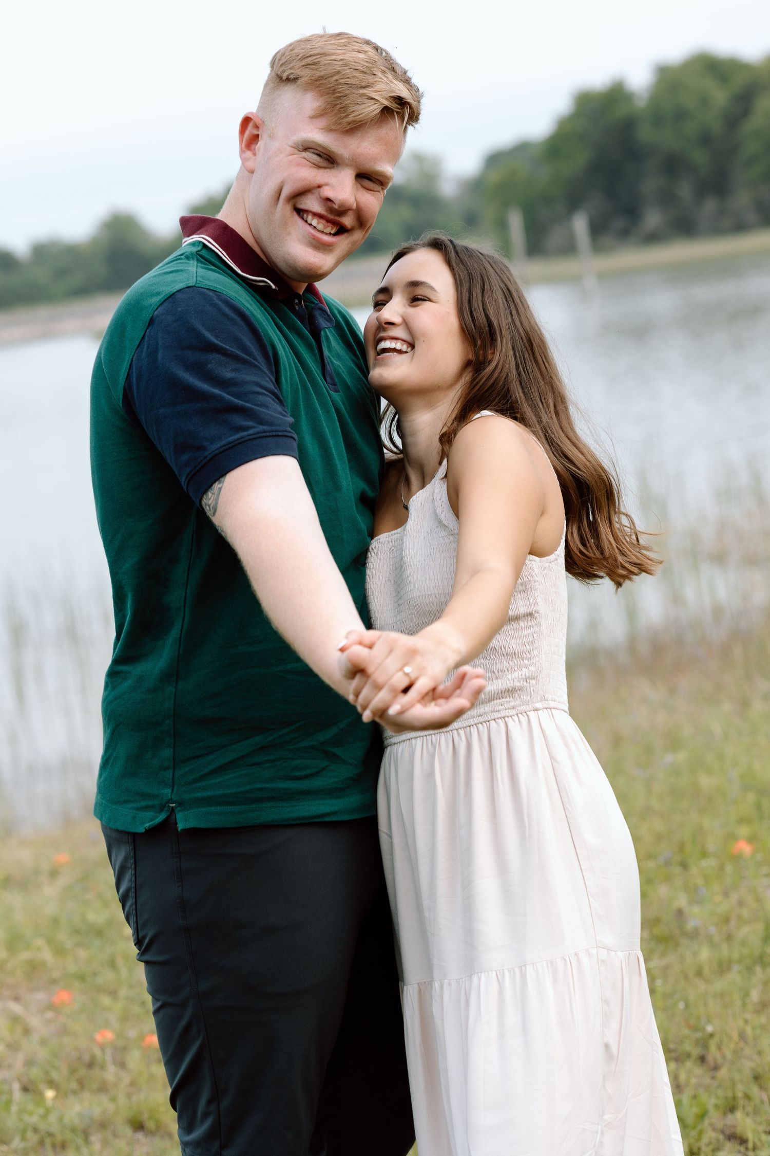 A playful couple shares a tender moment while standing in a field near a lake documentary photography college station Texas.