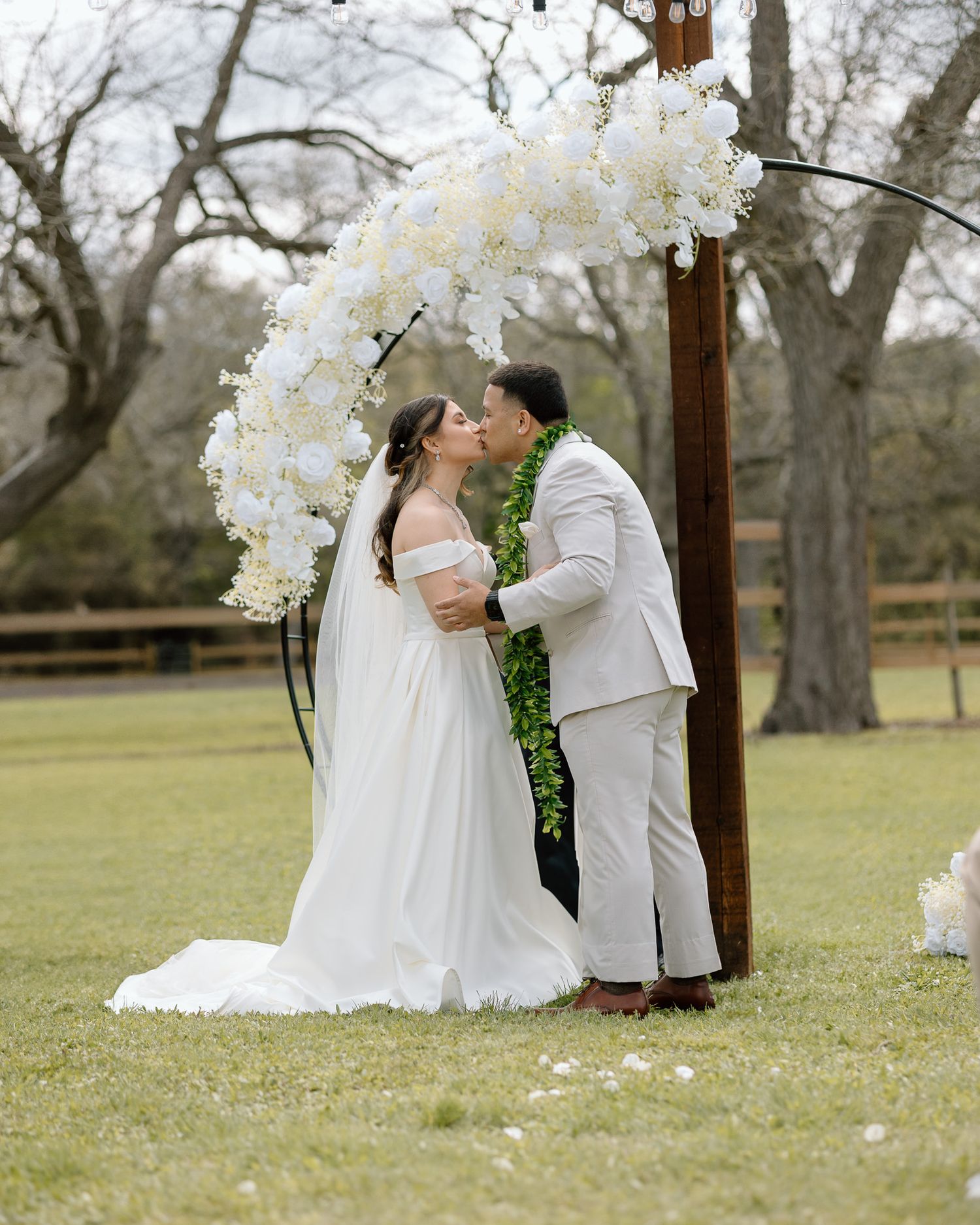 Elegant wedding ceremony beneath a curved arch adorned with white orchids in a garden setting.
