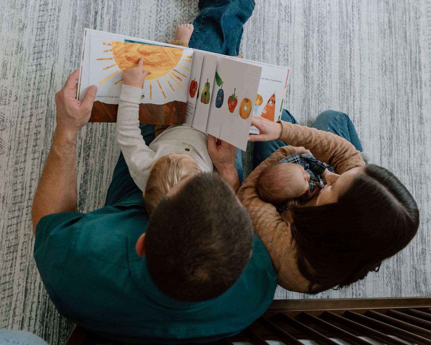 Overhead view of two people reading a childrens book together while sitting on a wooden floor.
