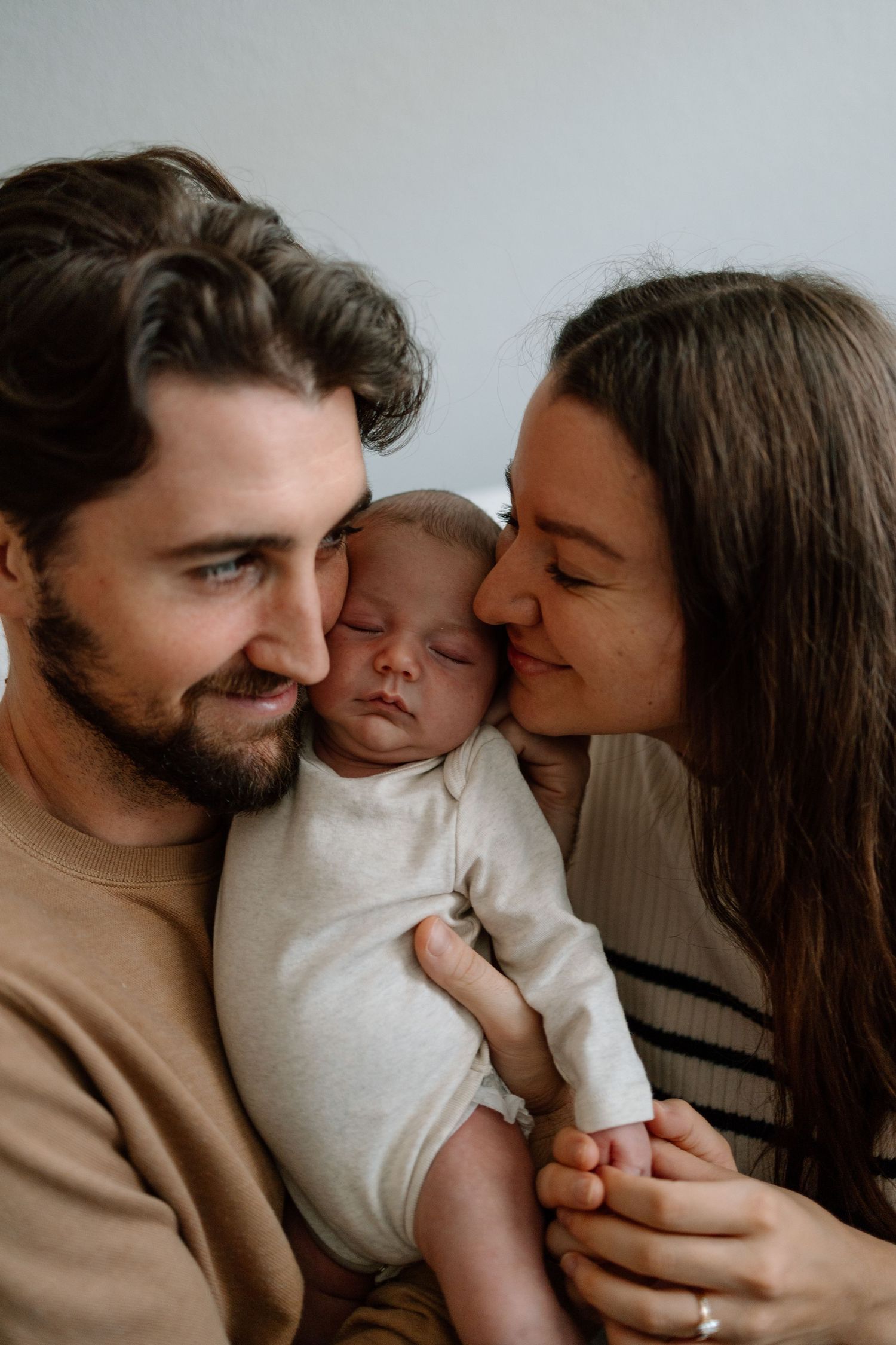 Sweet family moment with newborn baby being cradled and kissed by parents.