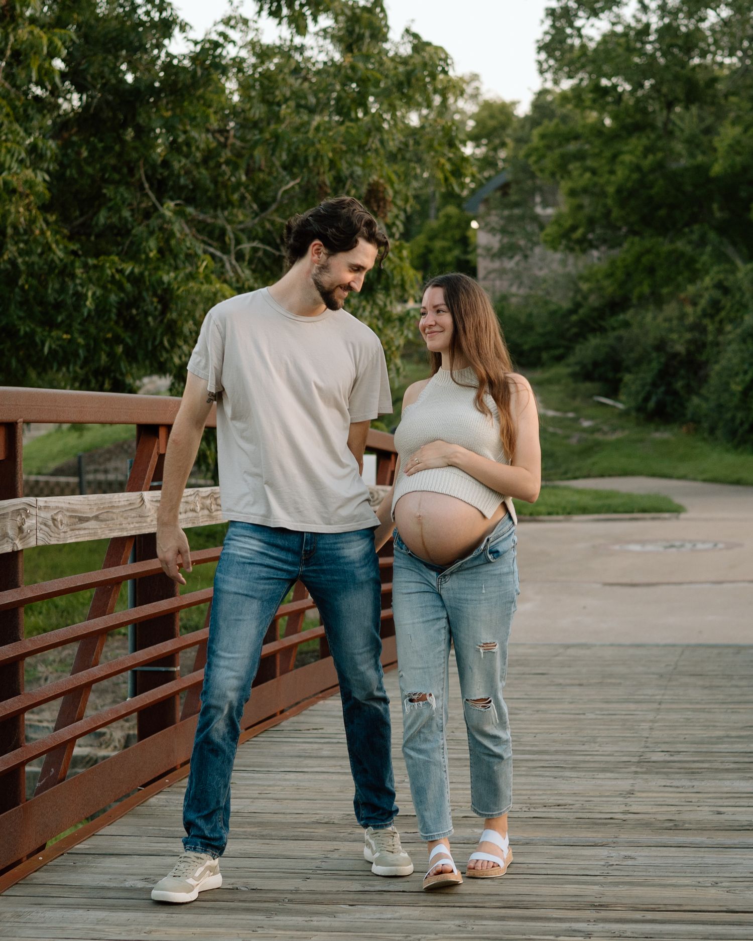 A couple shares an intimate moment on a wooden bridge during a maternity photoshoot.