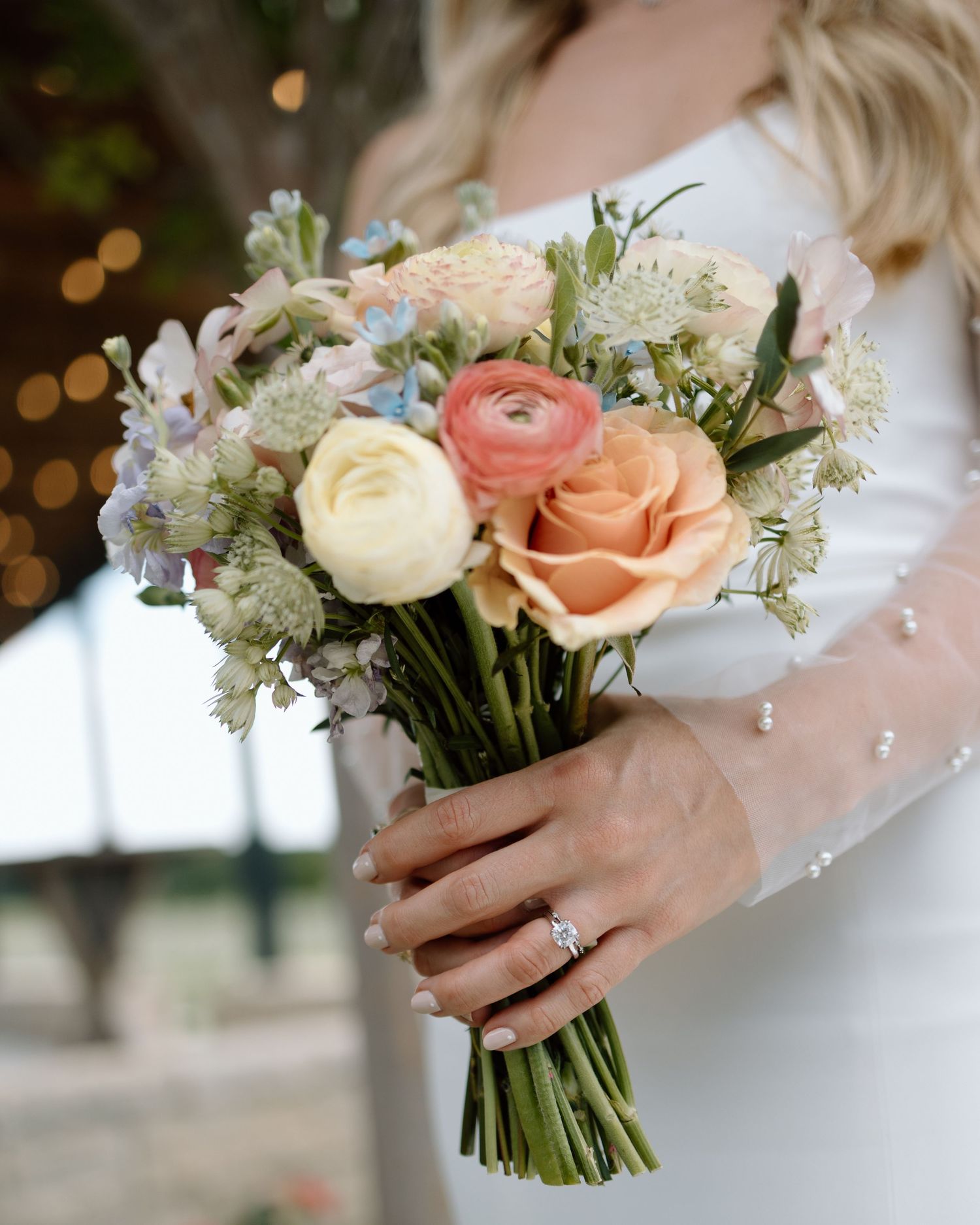 Bridal bouquet of peach, white and coral roses with delicate greenery and engagement ring.