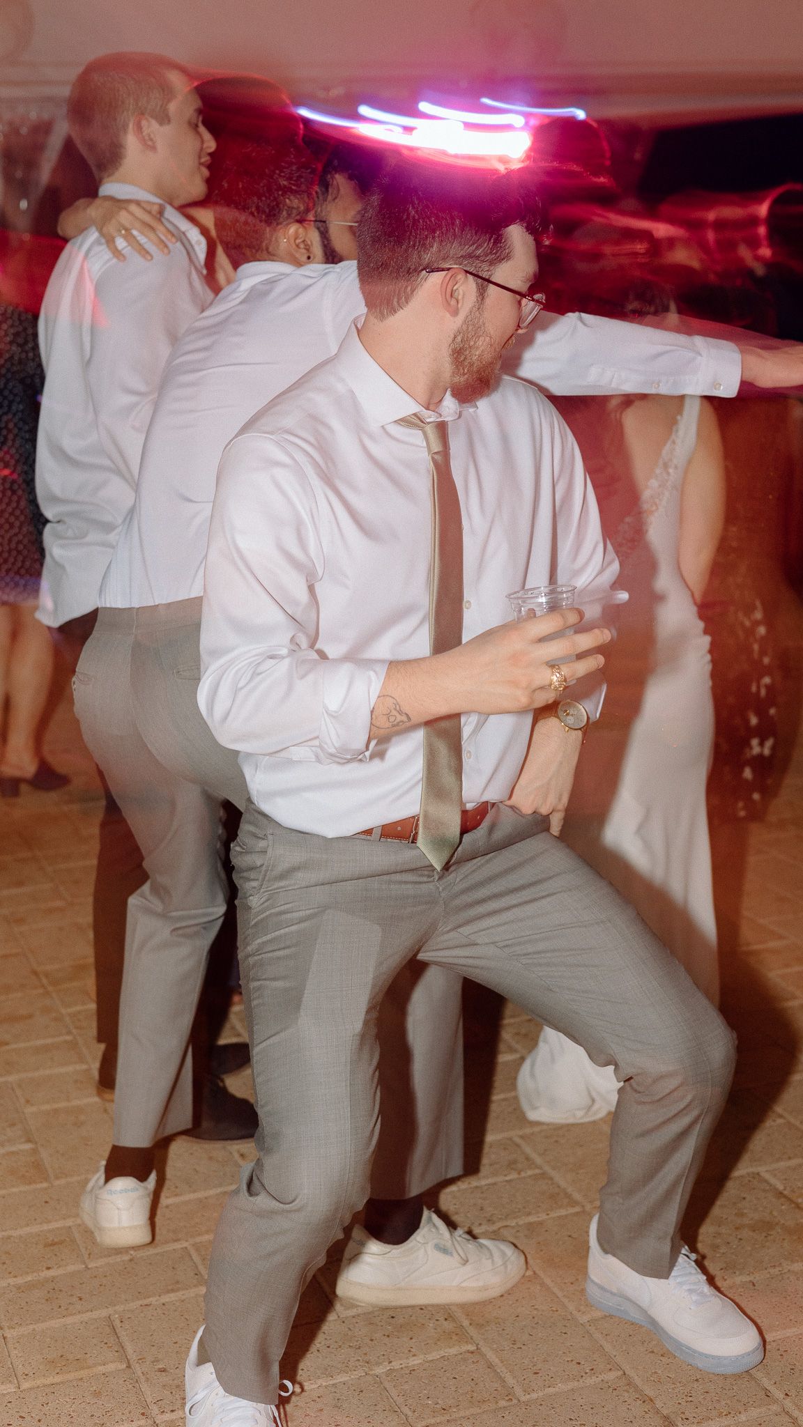 Wedding guest dancing energetically at reception with neon lights in background.