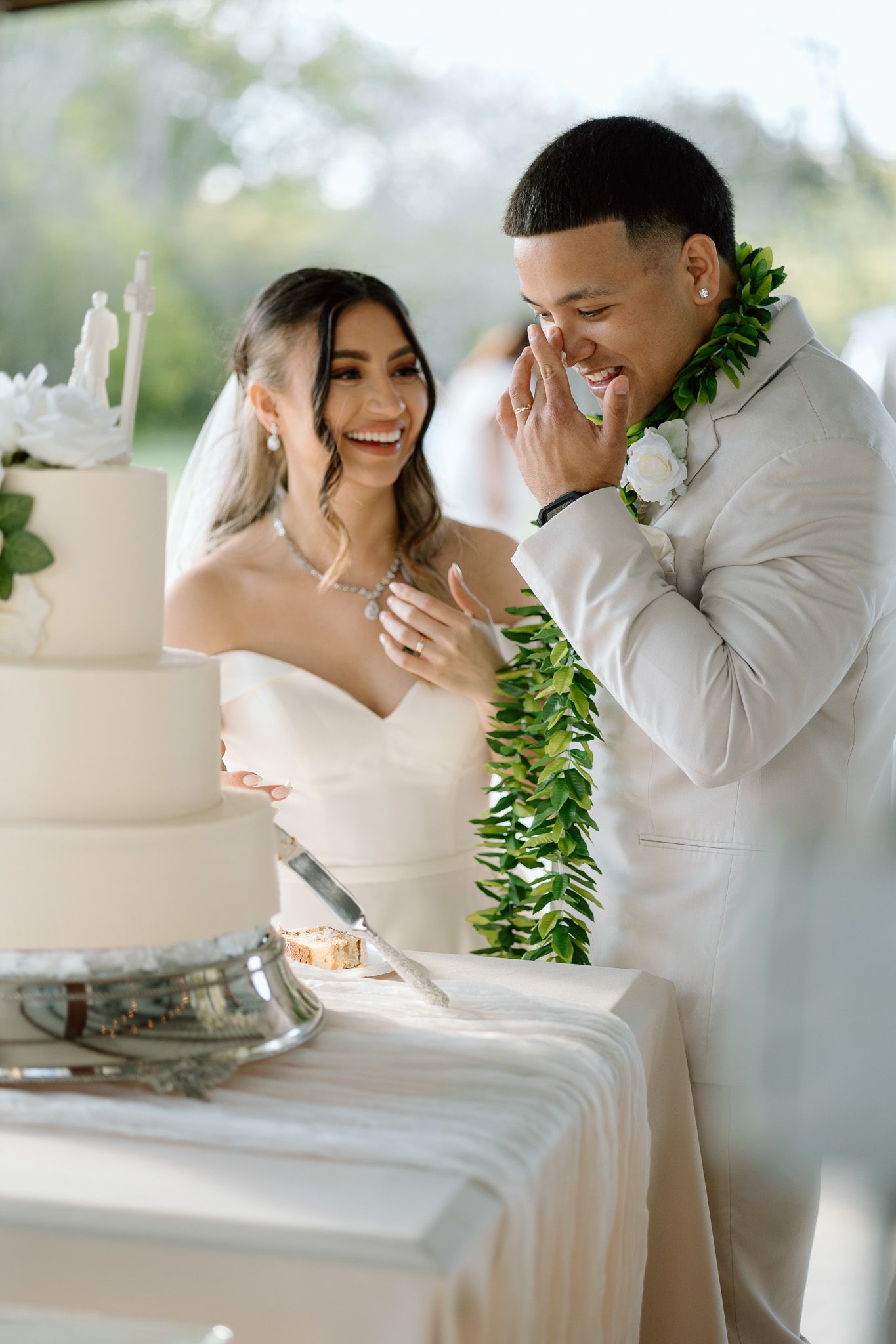 Newlyweds share laughter during cake cutting ceremony at outdoor wedding reception.