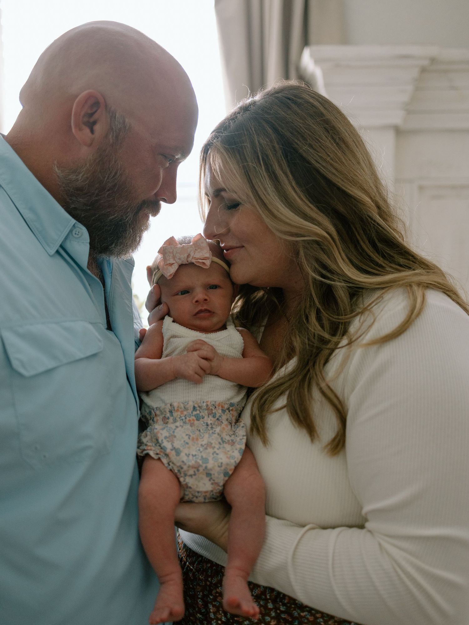 A couple shares an intimate moment with their newborn baby in a tender indoor family portrait.