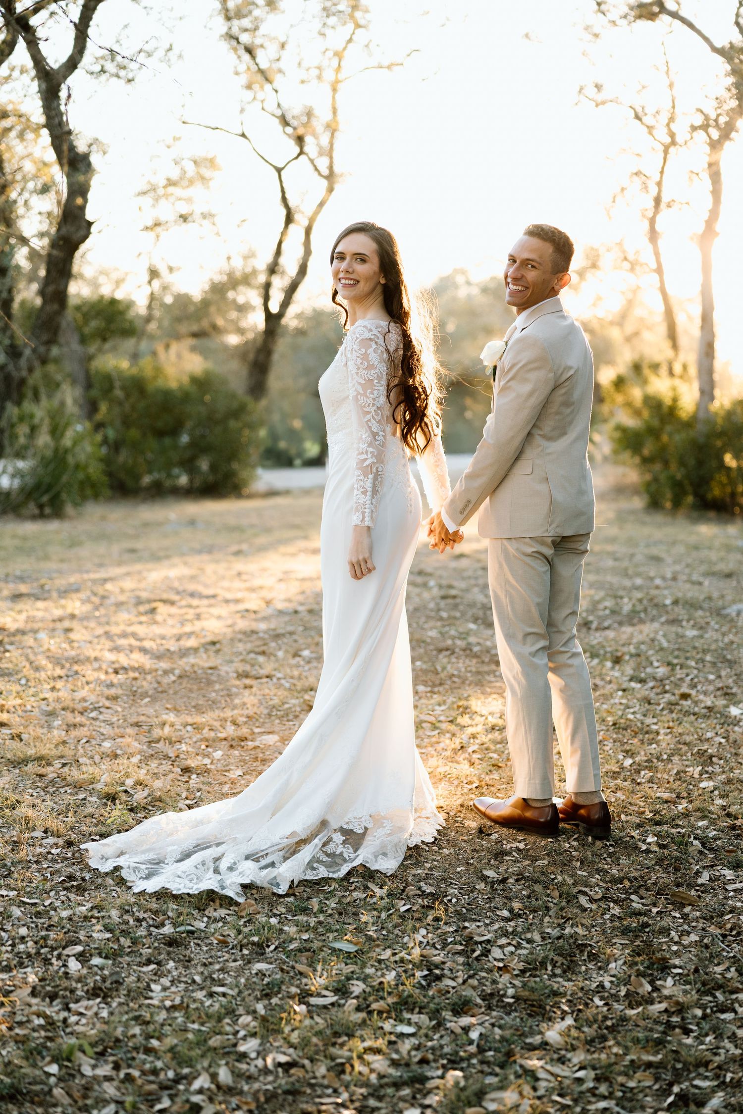 Bride and groom holding hands at golden hour in wooded outdoor wedding venue setting.
