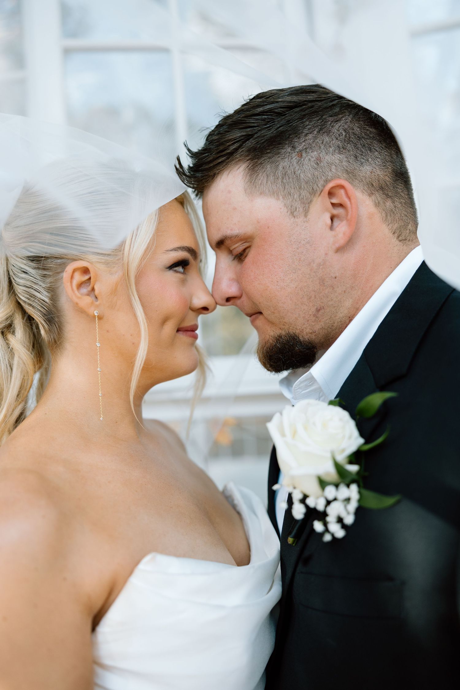 Bride and groom sharing an intimate forehead-to-forehead moment under a flowing white veil.