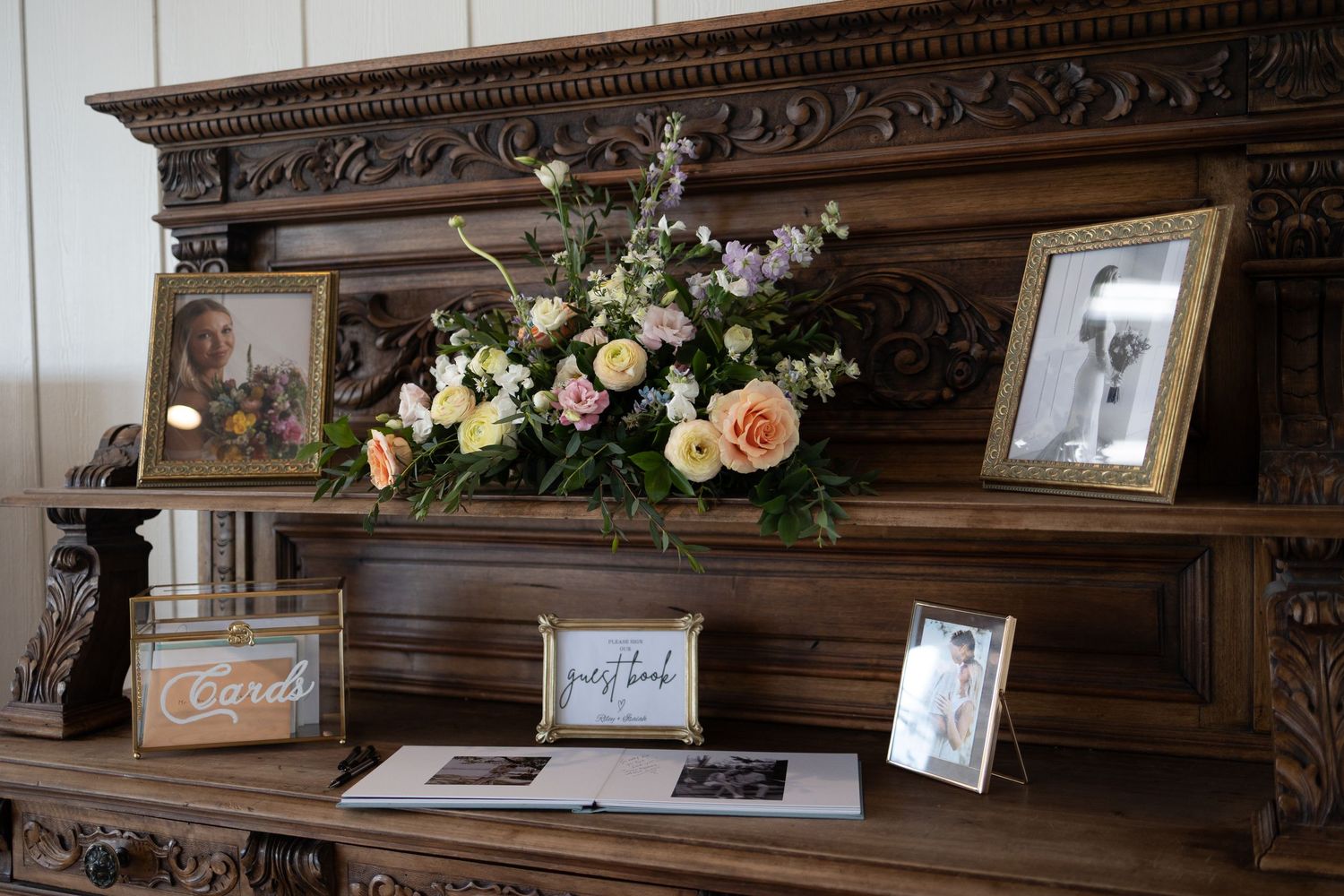 An ornate wooden mantel decorated with framed photos and floral arrangements for a wedding.