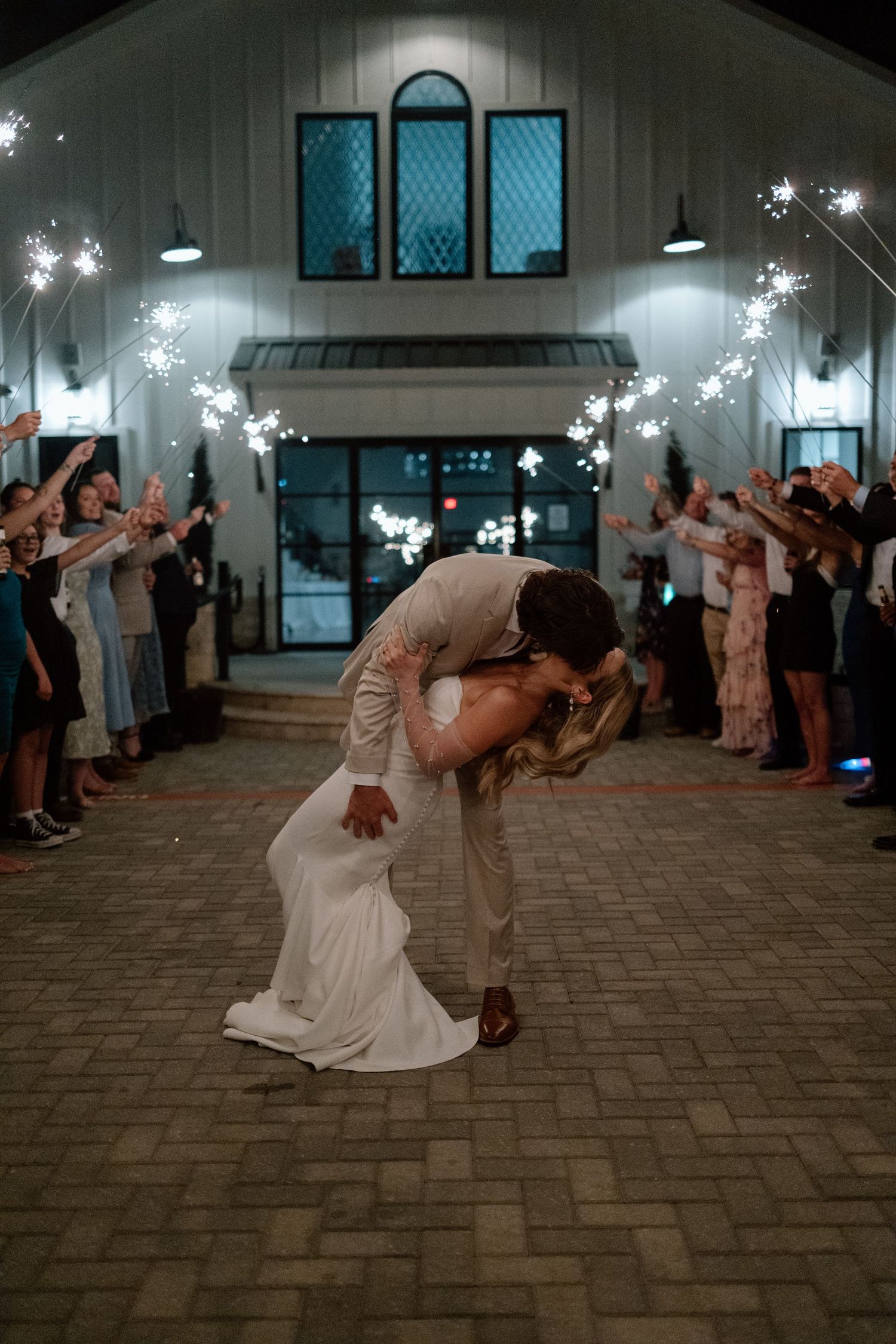 Romantic dip kiss under sparkler exit at evening wedding ceremony.
