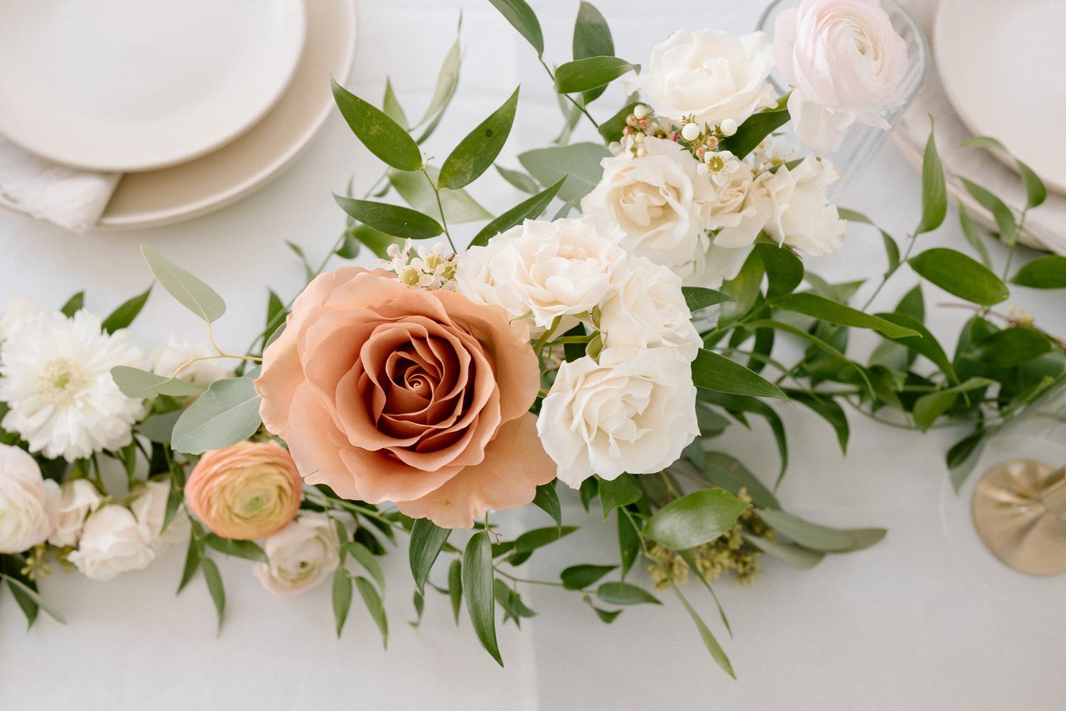 Elegant floral arrangement with peach roses and white flowers on a table setting.