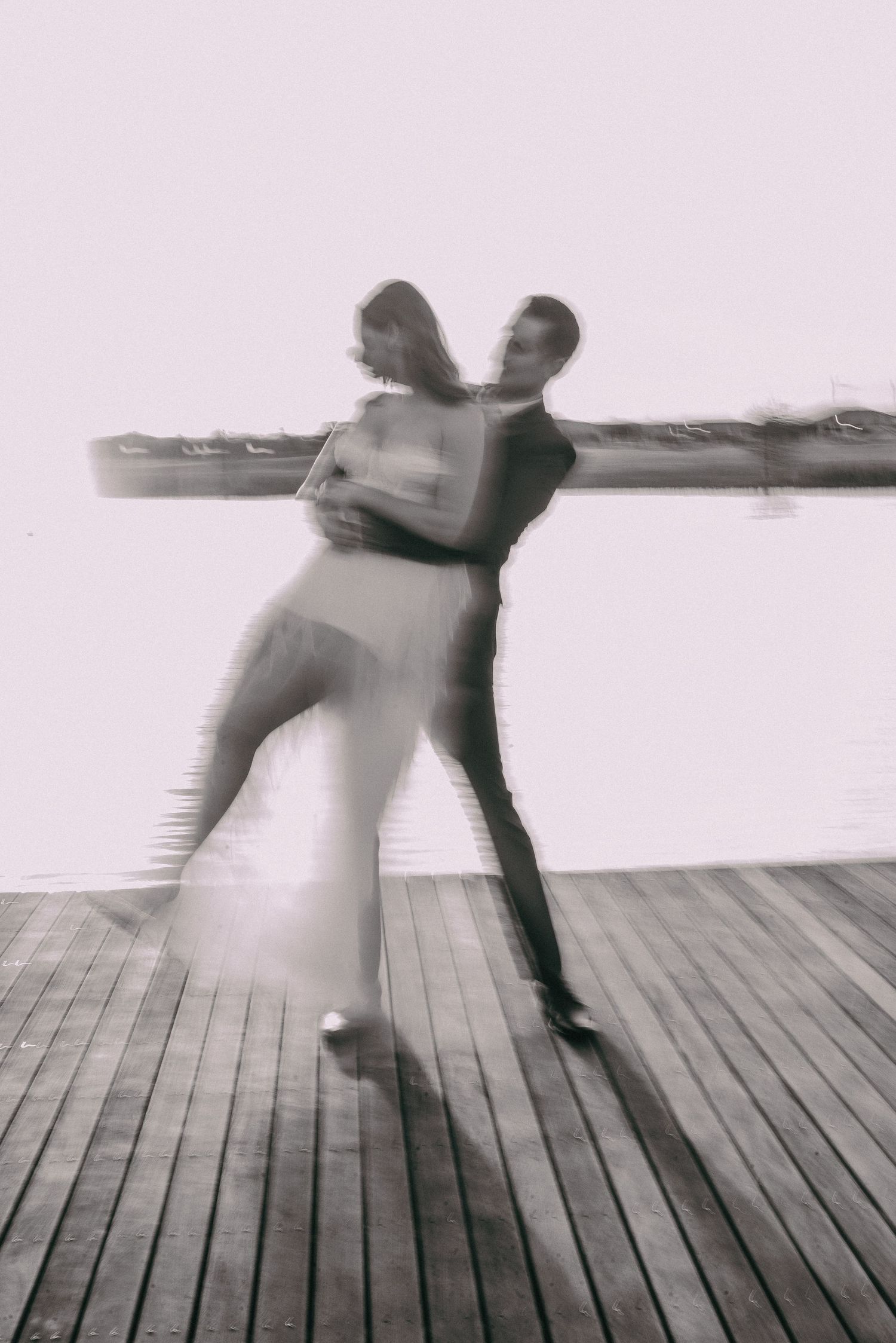 A black and white motion blur photo of two people dancing on a wooden deck.
