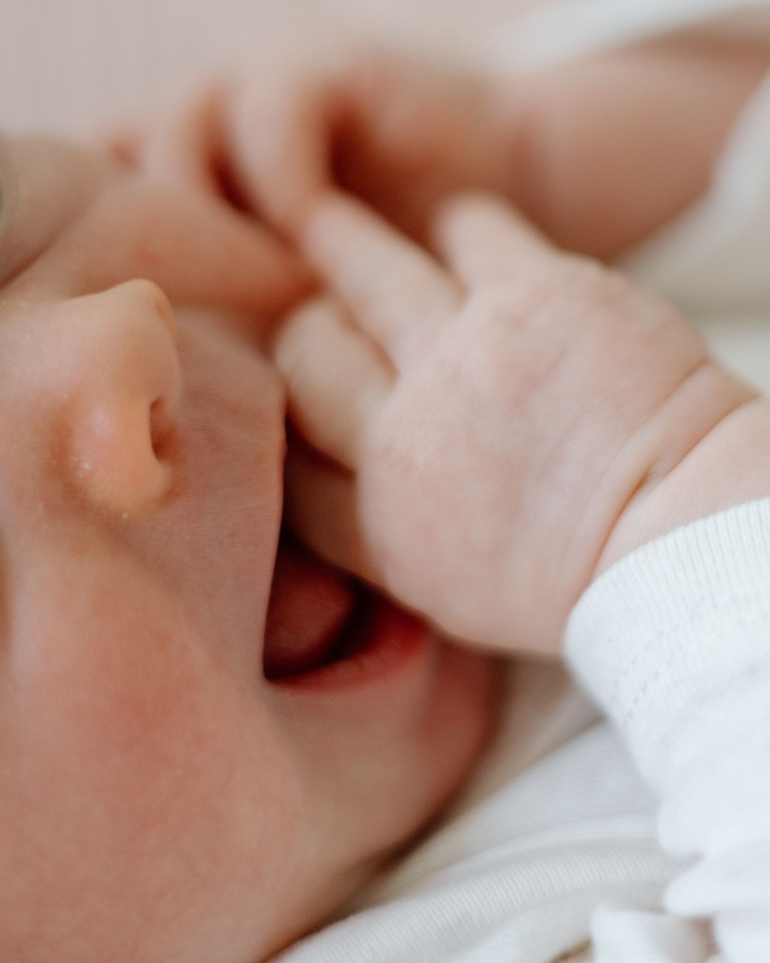 Close-up of baby's face with tiny hand reaching up.