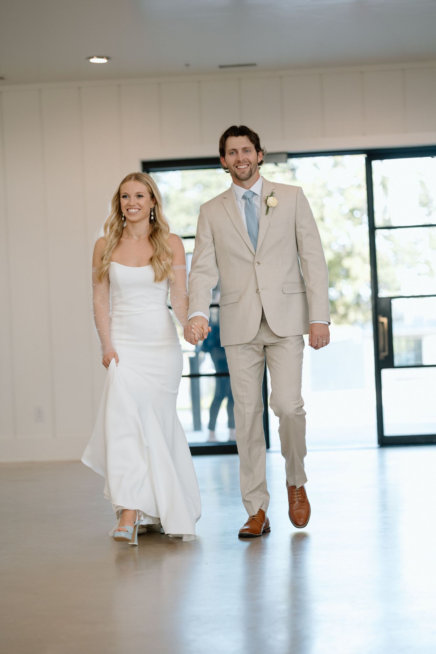 A wedding couple walks together in a bright indoor venue.