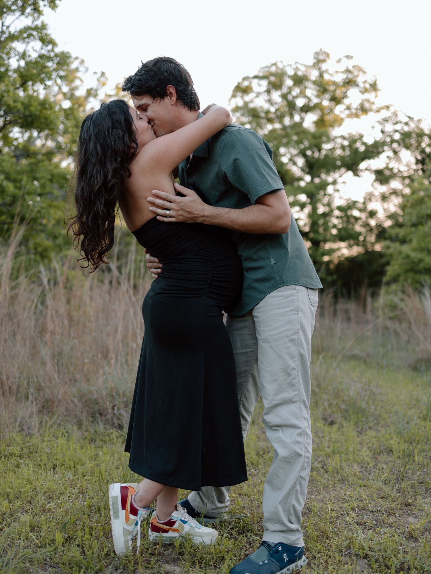 Romantic couple sharing a tender moment while standing in a grassy field at dusk.