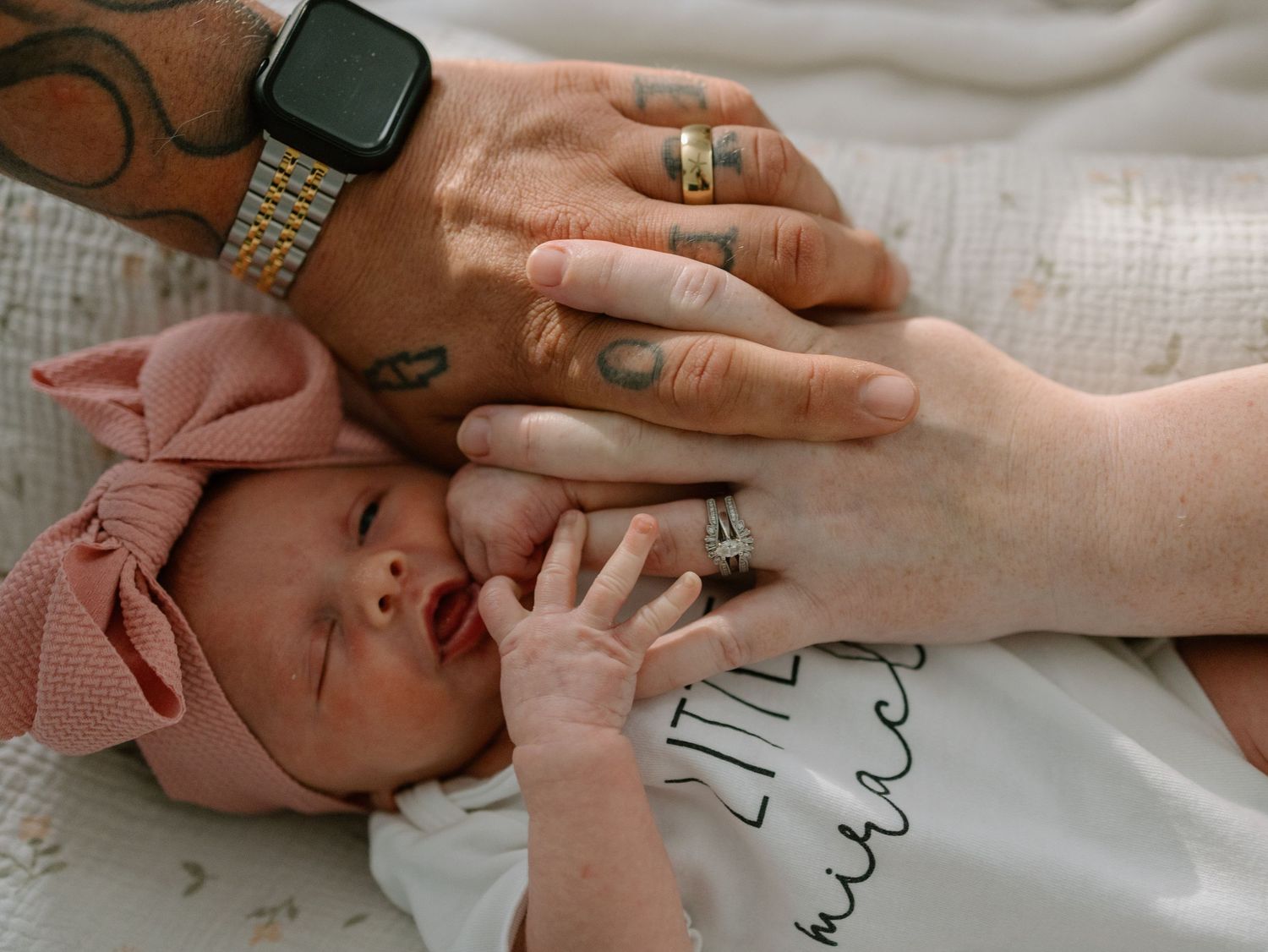 A tender moment captured as tiny baby hands touch adult hands wearing rings and a smartwatch.