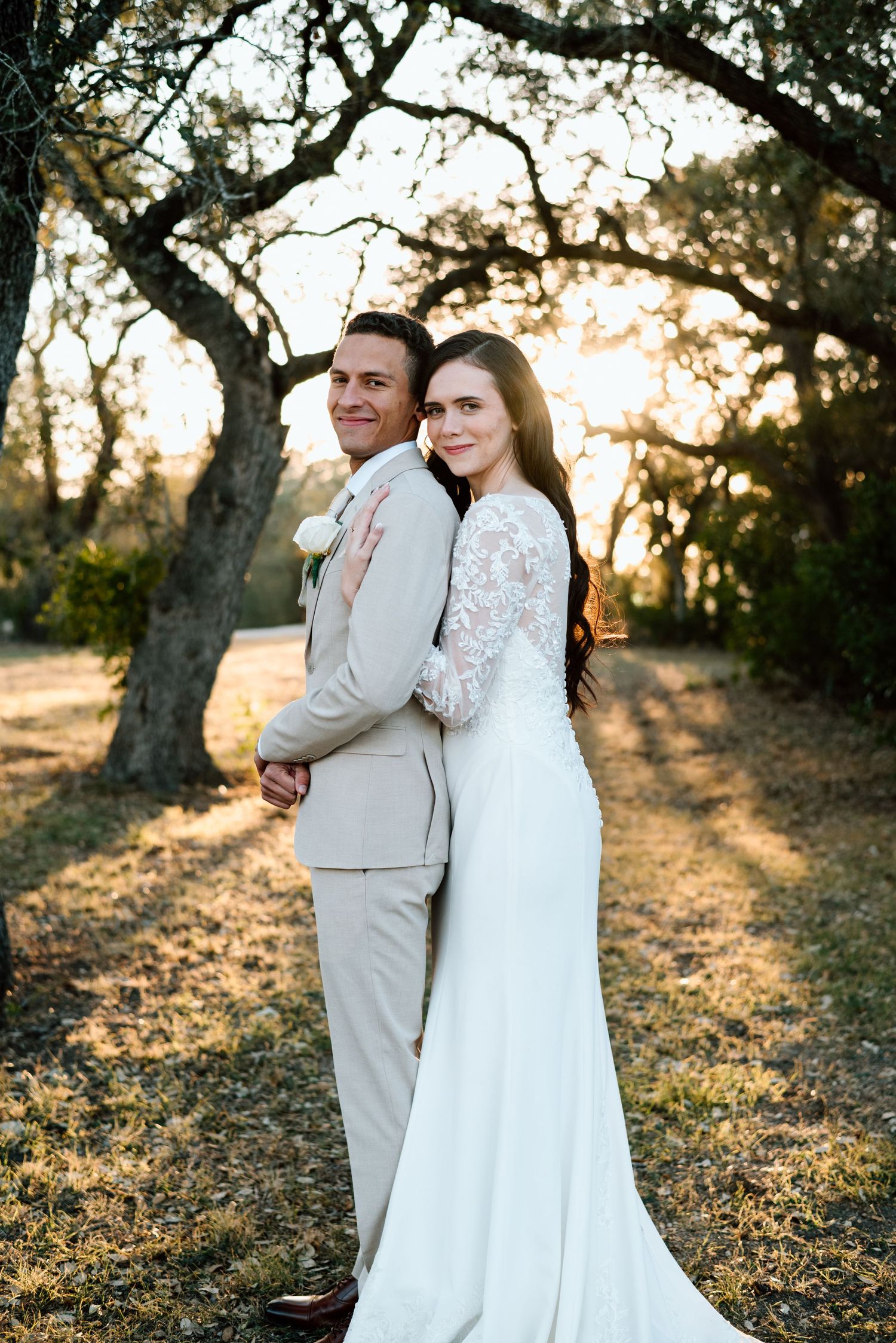 Bride and groom posing romantically under oak trees at golden hour sunset.