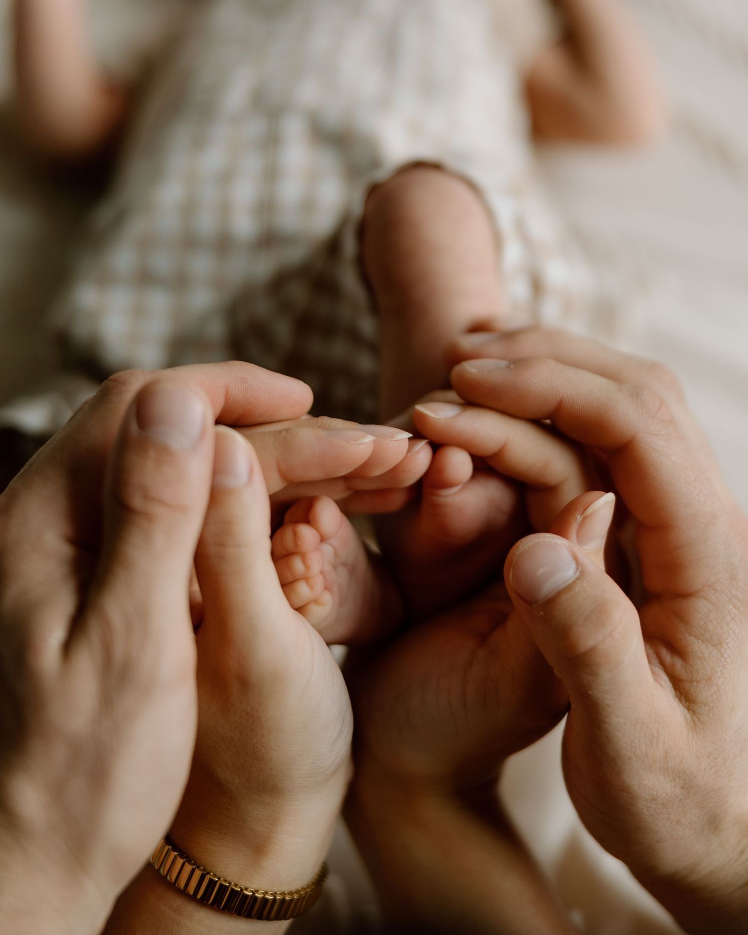Parents tenderly holding their newborn babys tiny feet and hands in a close-up photo.