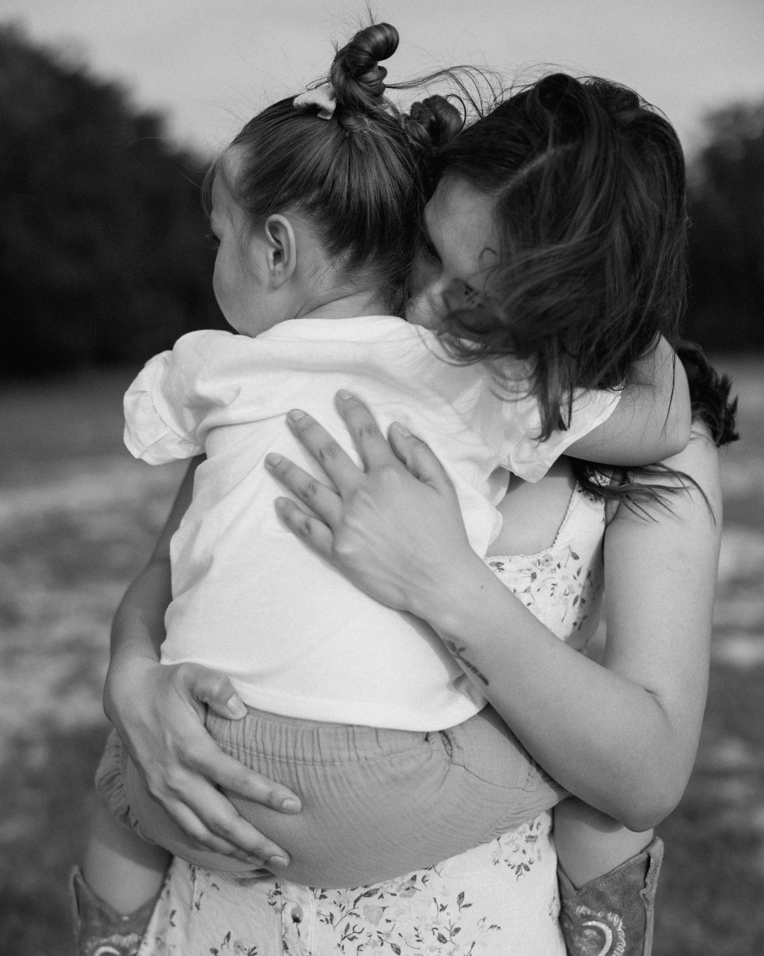 Black and white photo of a mother tenderly embracing her young toddler outdoors, sharing a loving moment.