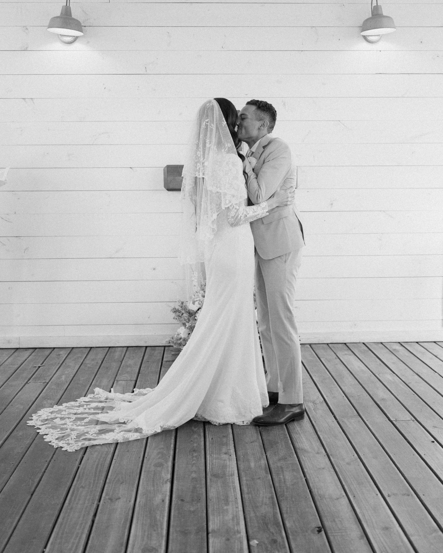 Black and white photo of bride and groom sharing first kiss on wooden deck at barn venue.