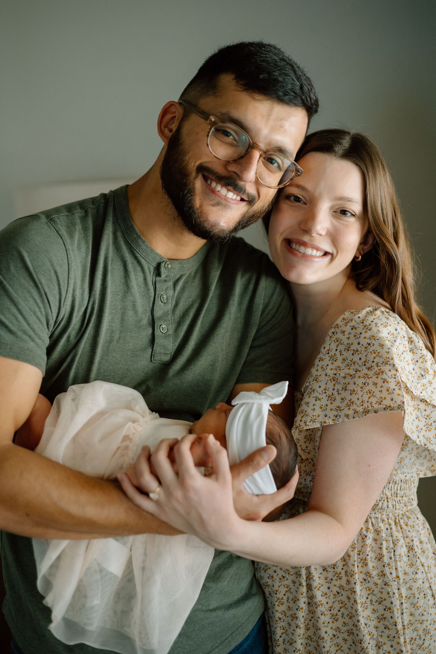Happy couple holding newborn baby while posing together against gray background.