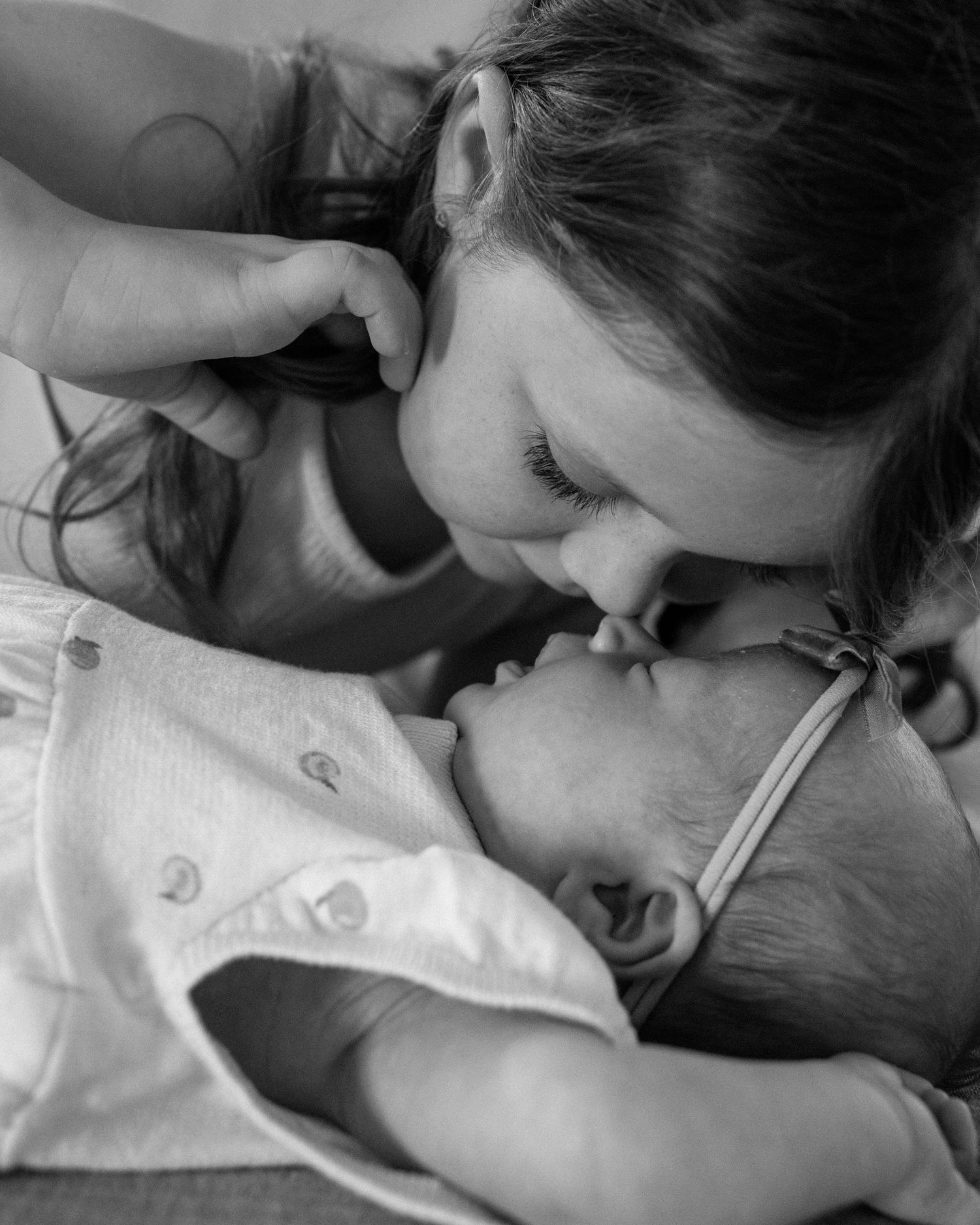 Black and white photo of a mother tenderly kissing her newborn baby, capturing a precious bonding moment.