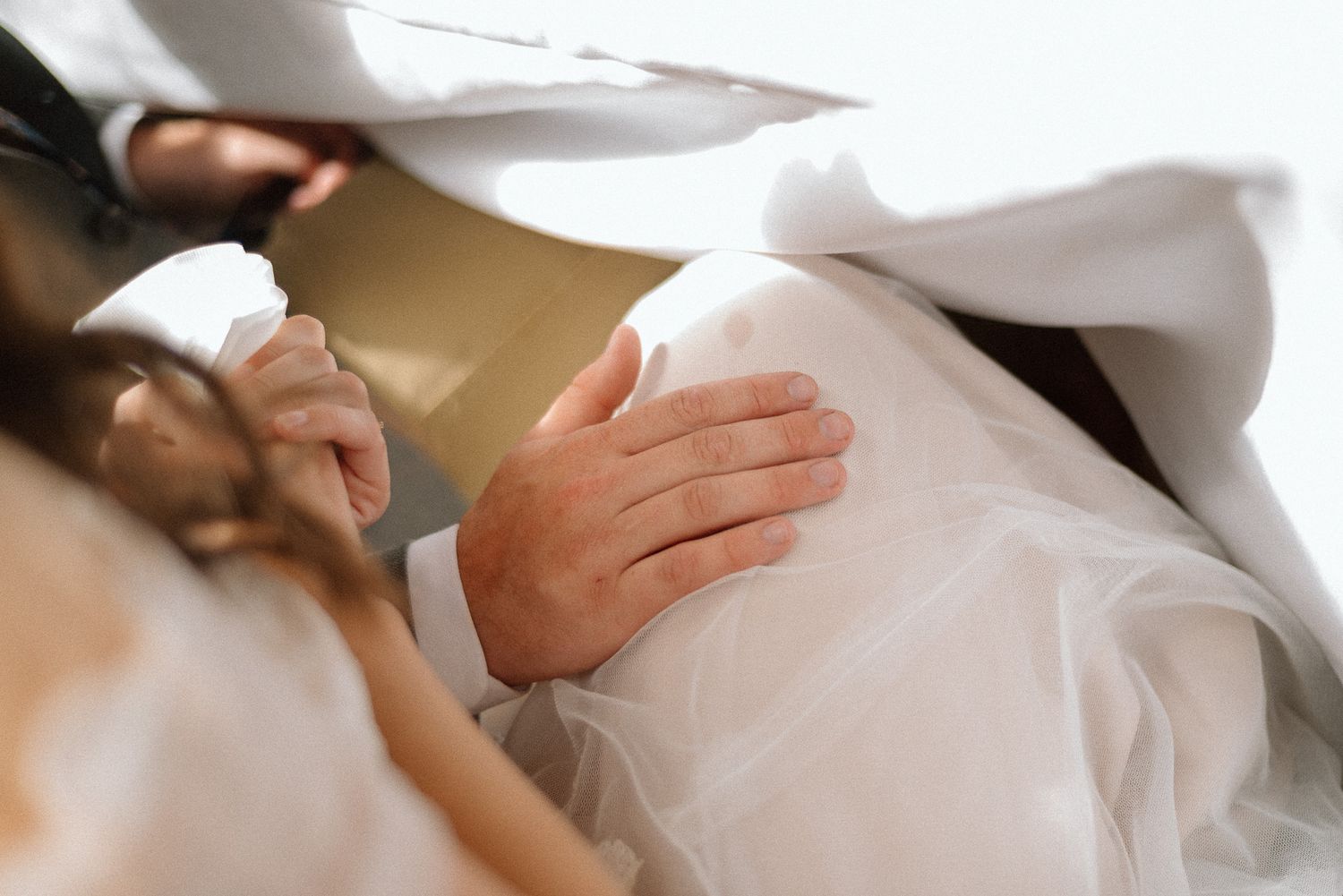 Close-up detail of delicate white wedding dress fabric and hands.