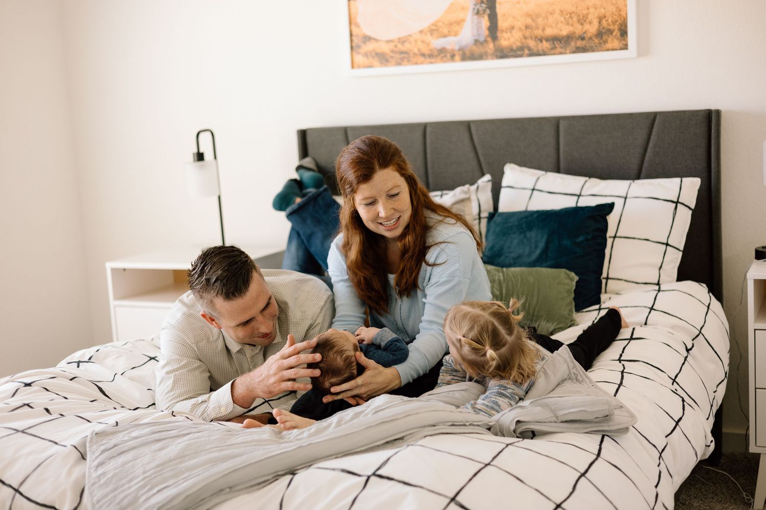 Family with young child and dog relaxing together on a bed with white bedding in a bright modern bedroom.
