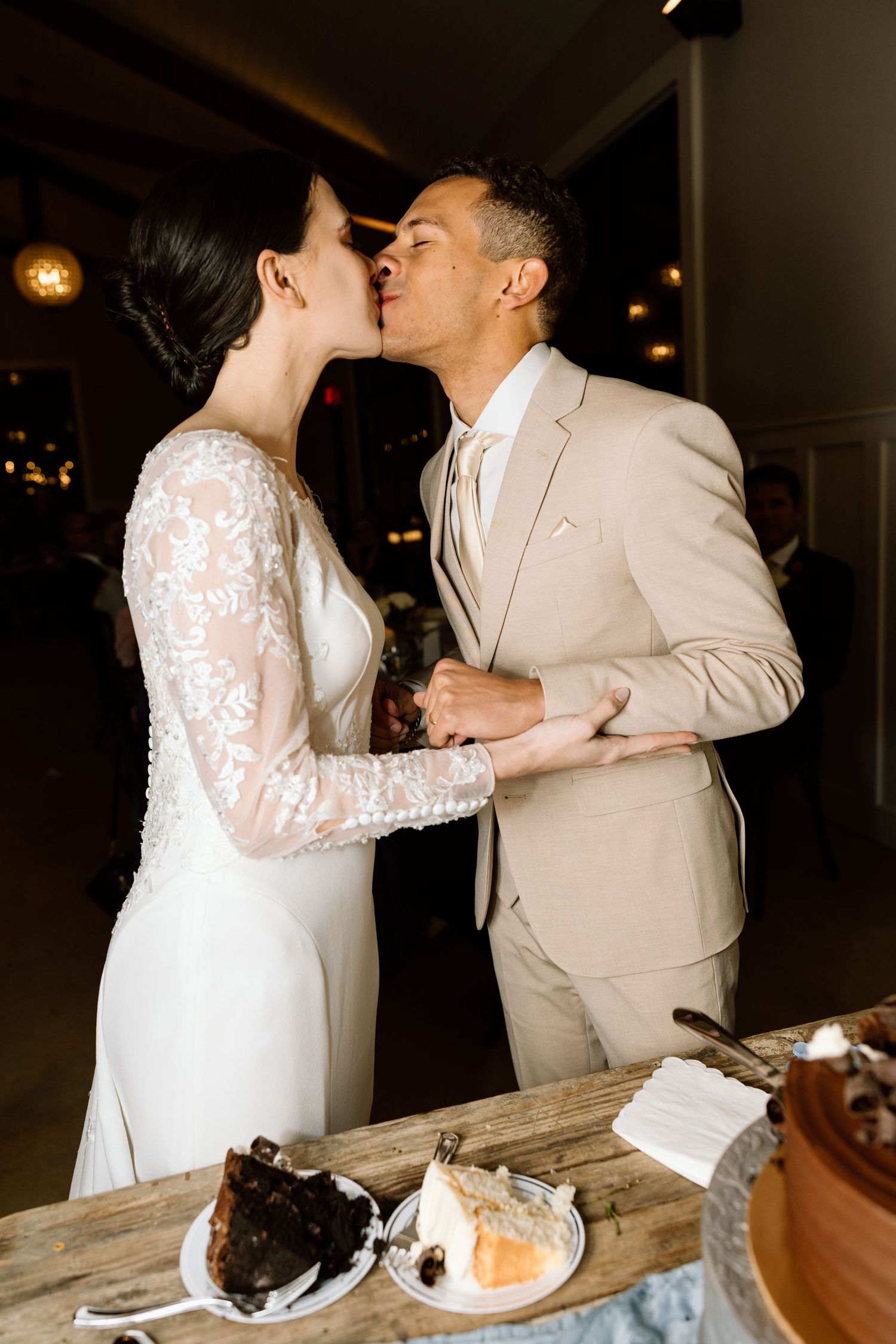 Bride and groom sharing a kiss while cutting their wedding cake at a romantic indoor reception.