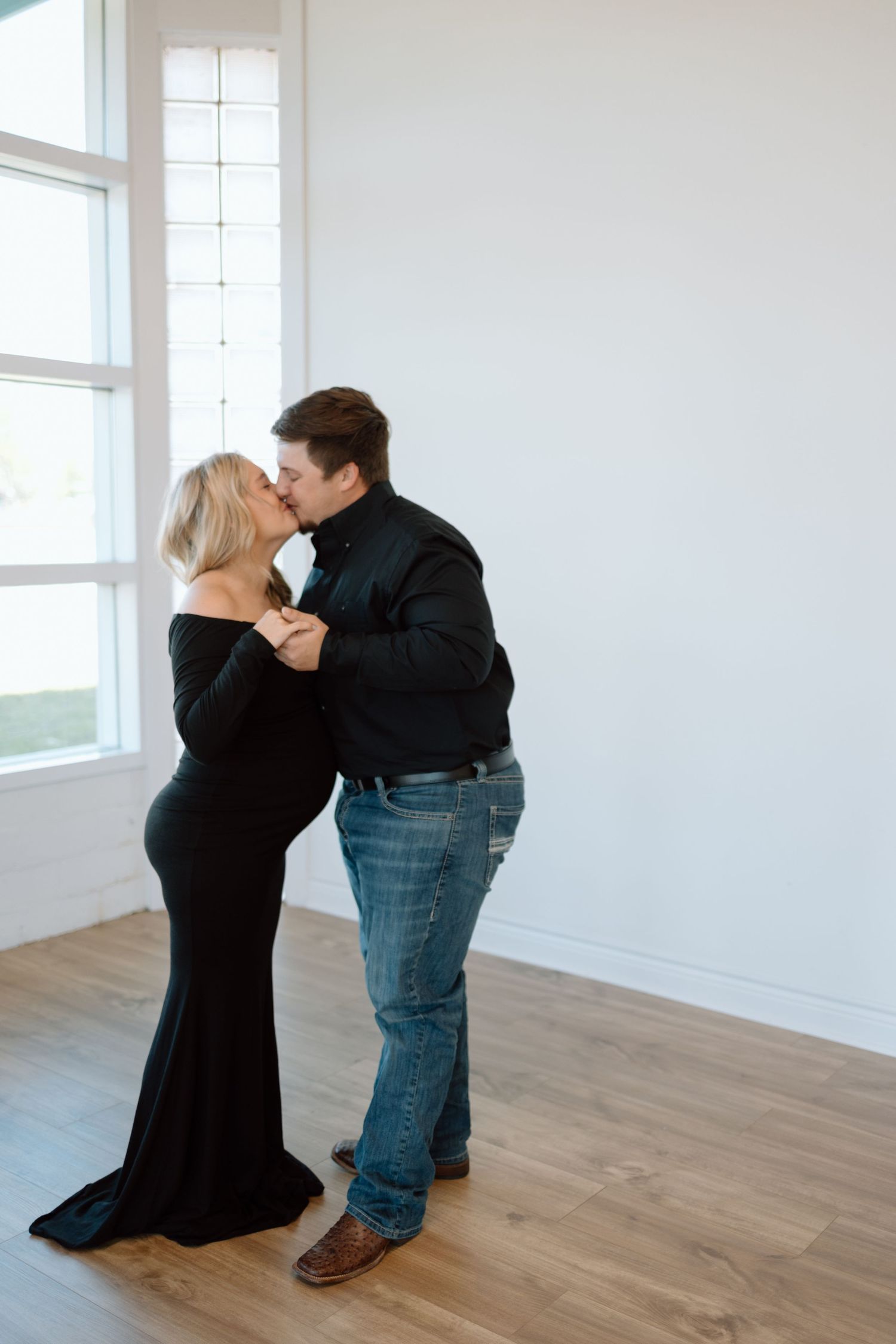 A couple share an intimate moment as they dance together in an open bright room with white walls and hardwood floors.