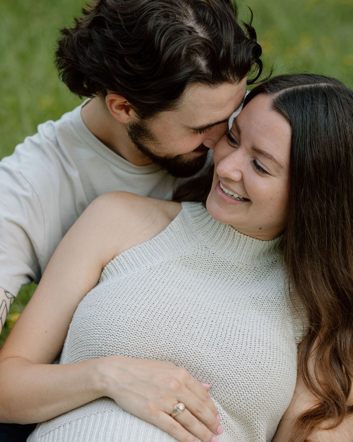 Intimate outdoor portrait of a couple embracing in a grassy field with soft natural lighting.