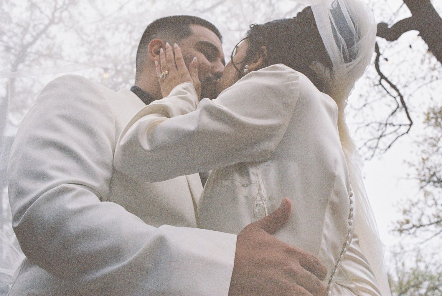 A tender wedding moment captured between two people in white attire against a misty background.