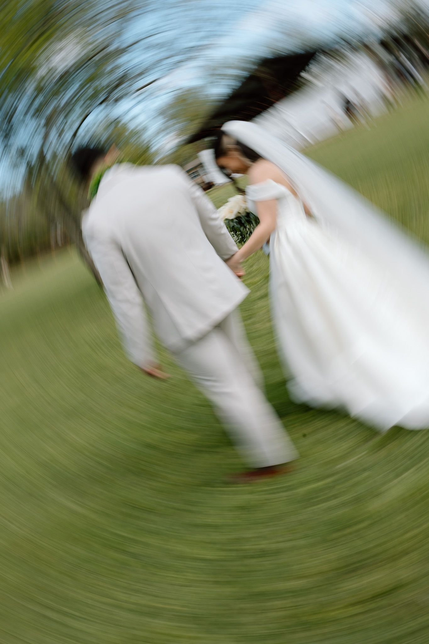Artistic motion blur photo of couple in white wedding attire spinning on grass.