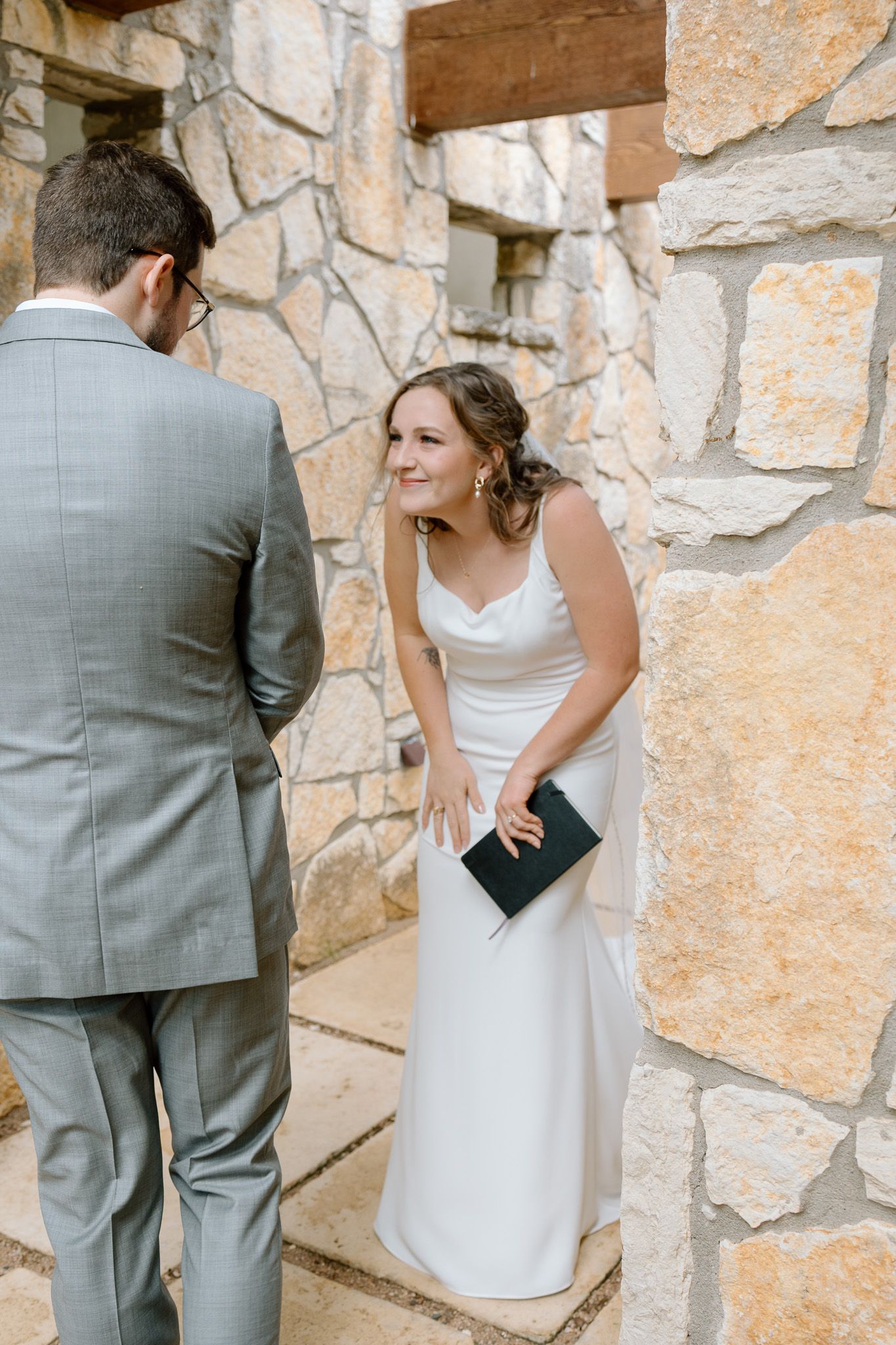 A wedding couple share a private moment against a rustic stone wall backdrop.