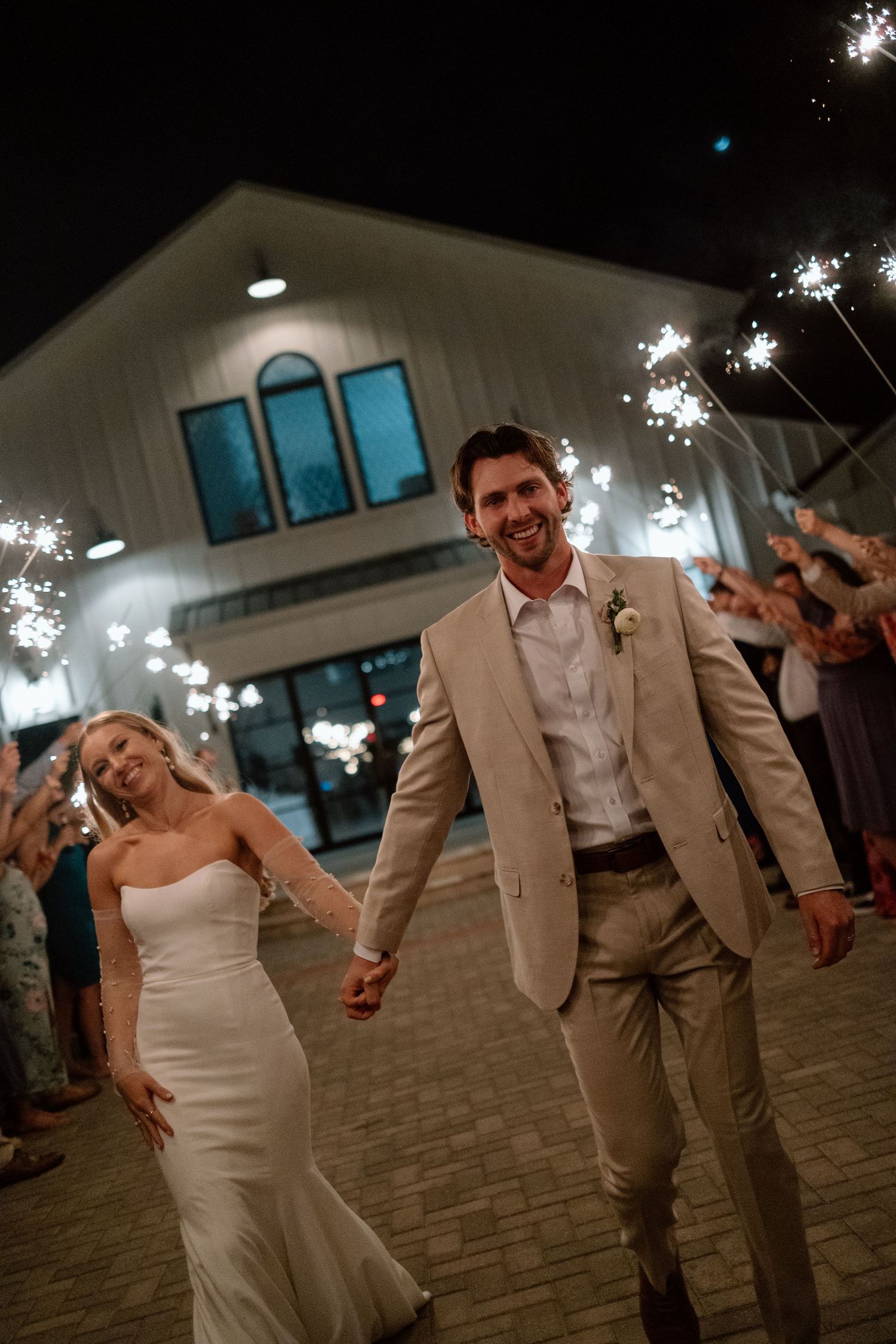 Couple celebrating under sparklers during evening wedding reception.