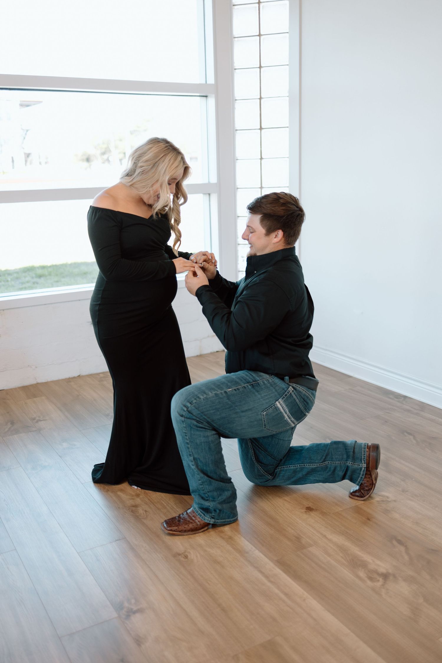 A proposal moment captured in a bright room with wooden floors as someone kneels on one knee presenting a ring.