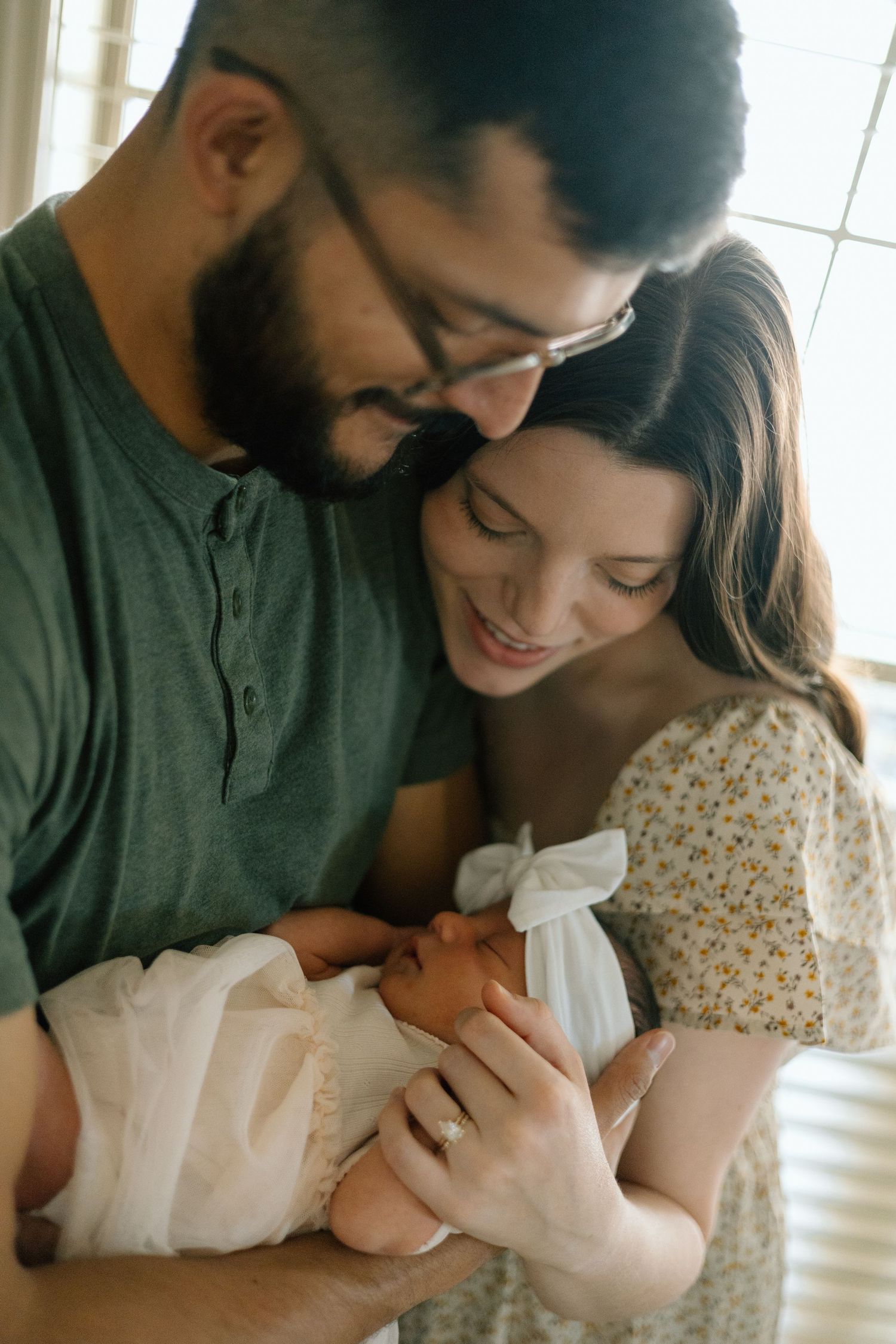 A couple gazes lovingly at their newborn baby wrapped in white swaddling cloth.