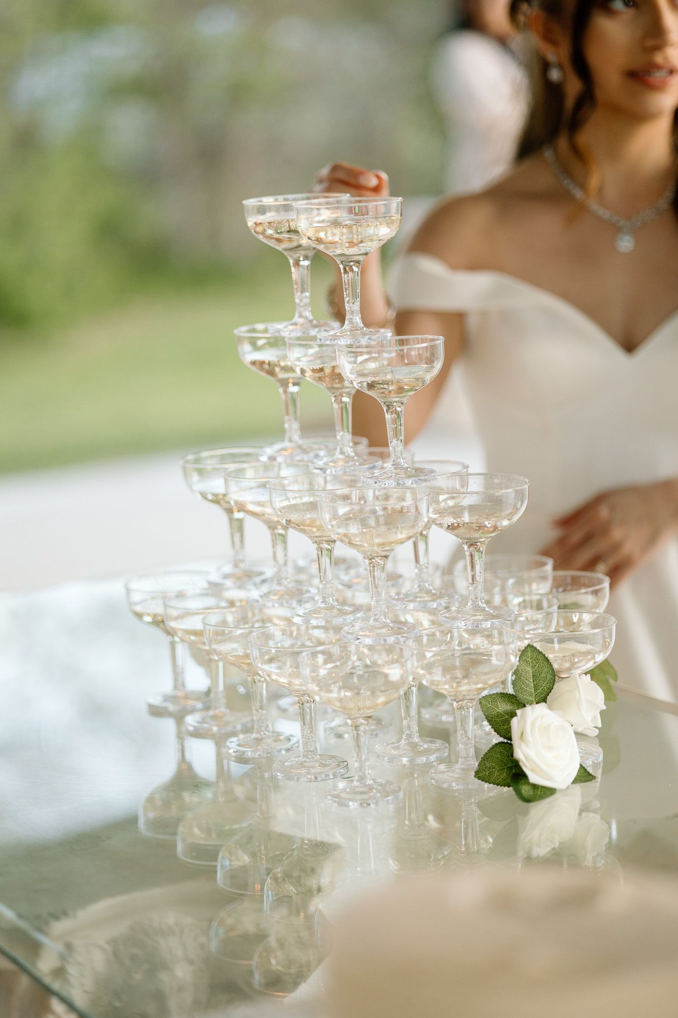 Elegant champagne tower with coupe glasses and white rose decoration at wedding reception.