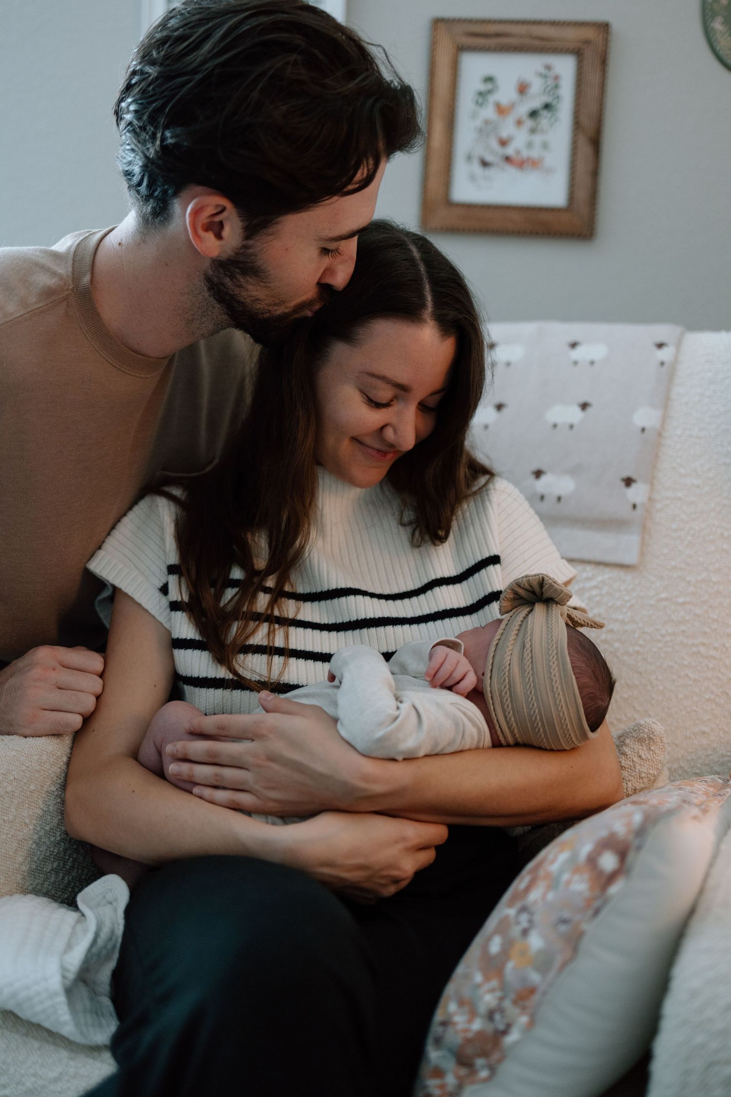 Intimate family moment on couch with newborn baby in white outfit.