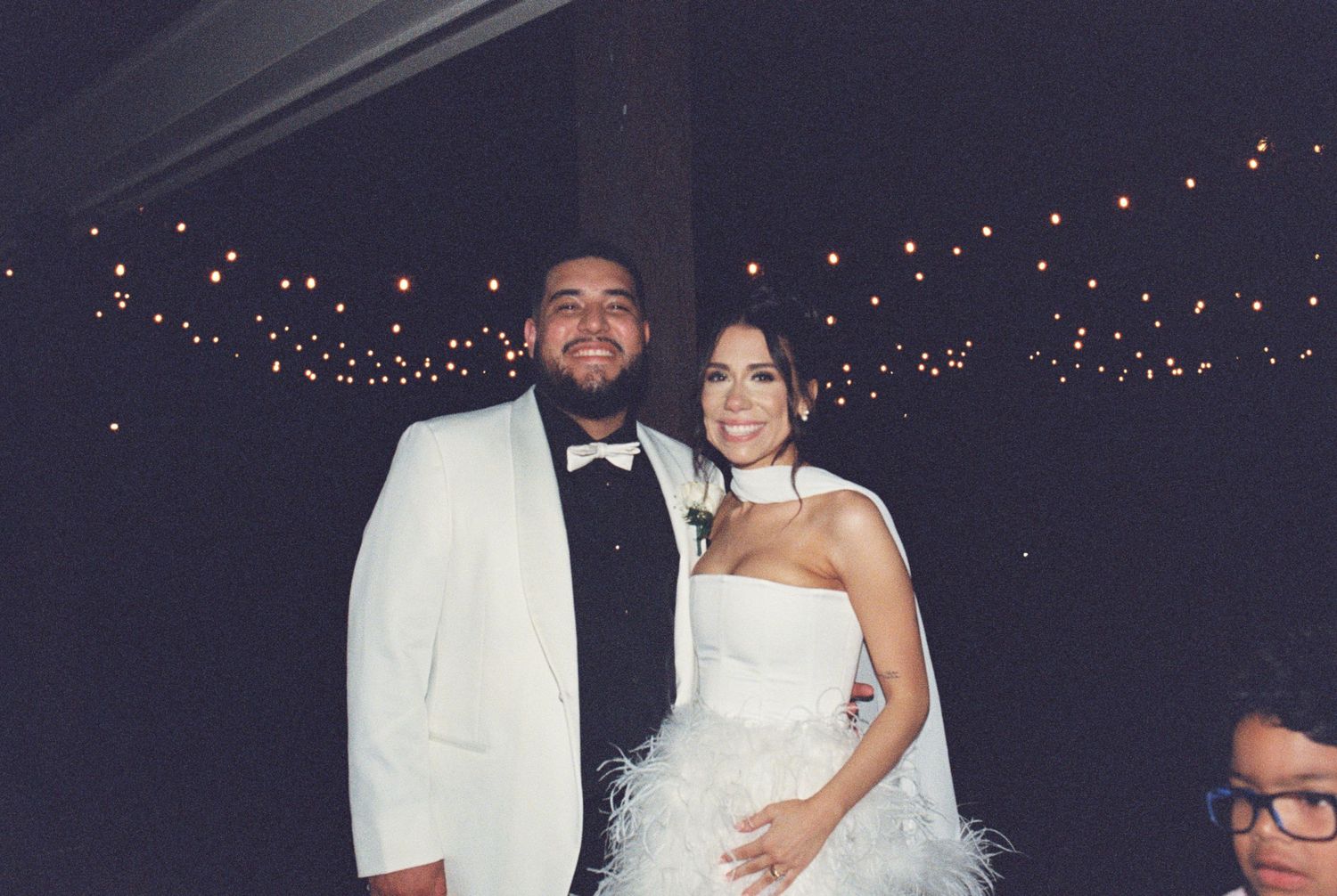 A couple poses together at their wedding reception under twinkling lights.