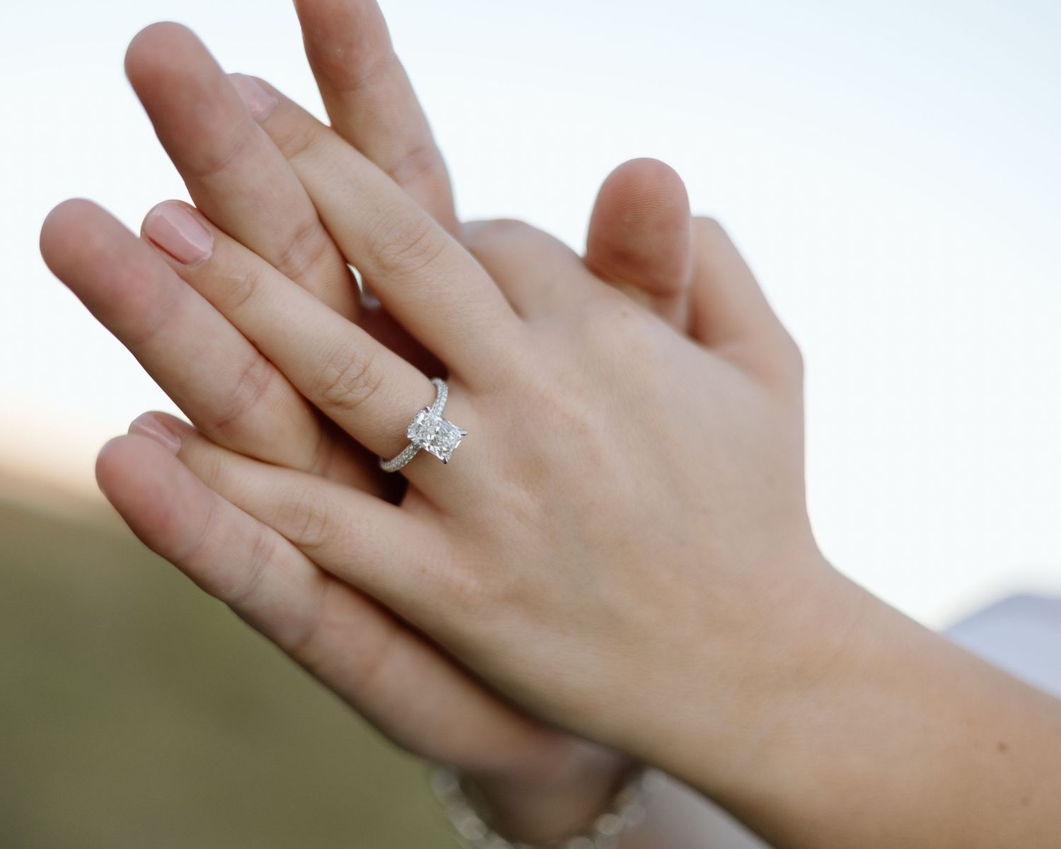 Close-up of two hands with a sparkling diamond solitaire engagement ring on the ring finger.