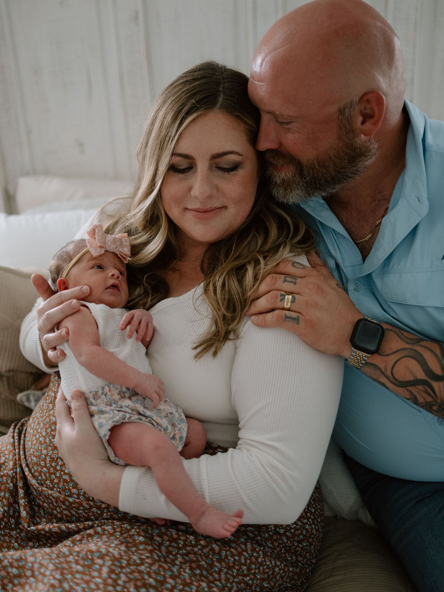 Intimate family portrait showing tender moment with newborn baby resting on floral blanket in soft natural light.