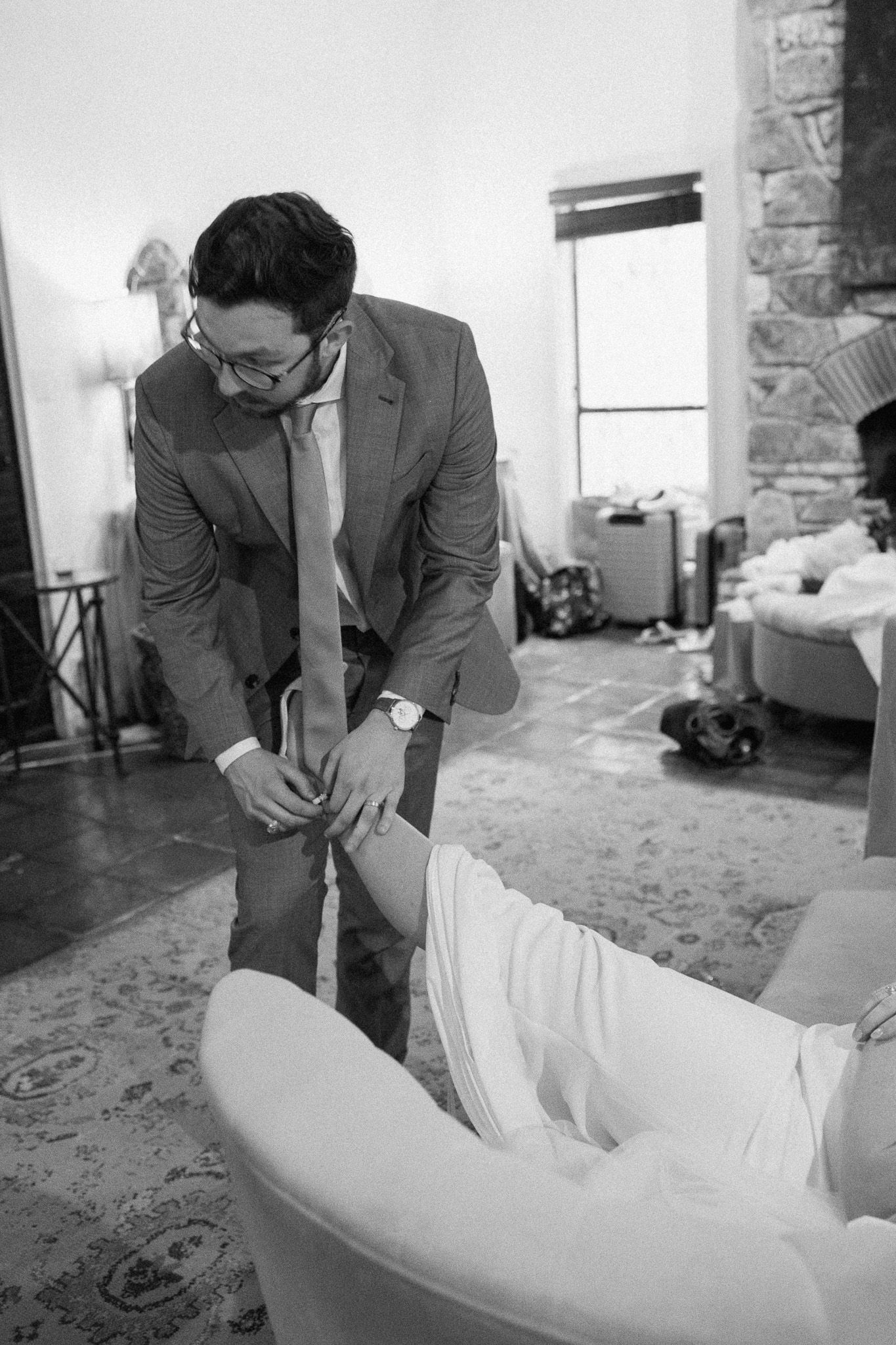 Bride receiving assistance with getting ready in a candid black and white moment during wedding preparations.