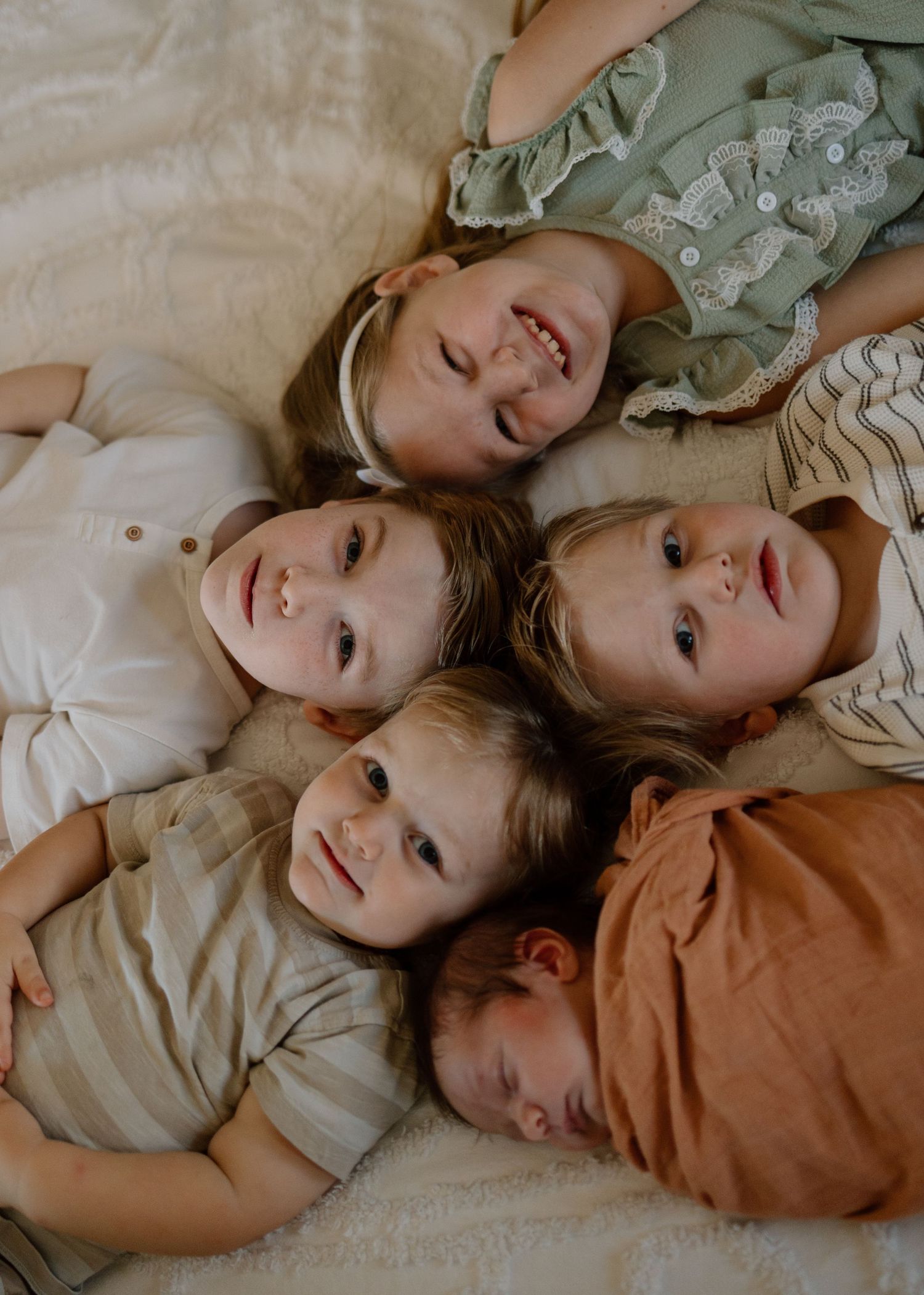 Group of children lying down together in a circle formation on a beige surface wearing casual clothing.