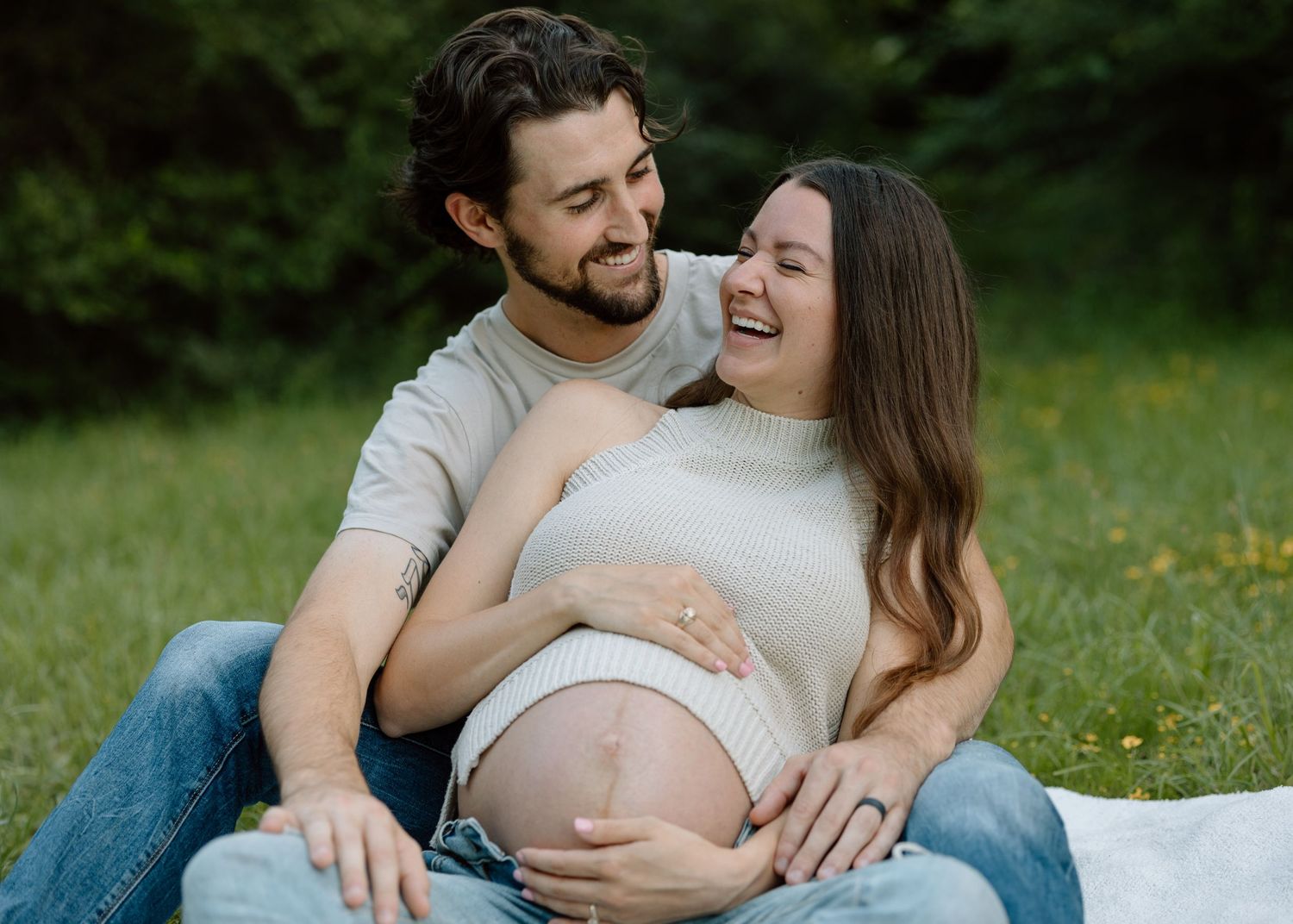 Joyful outdoor maternity portrait with couple sitting on grass.